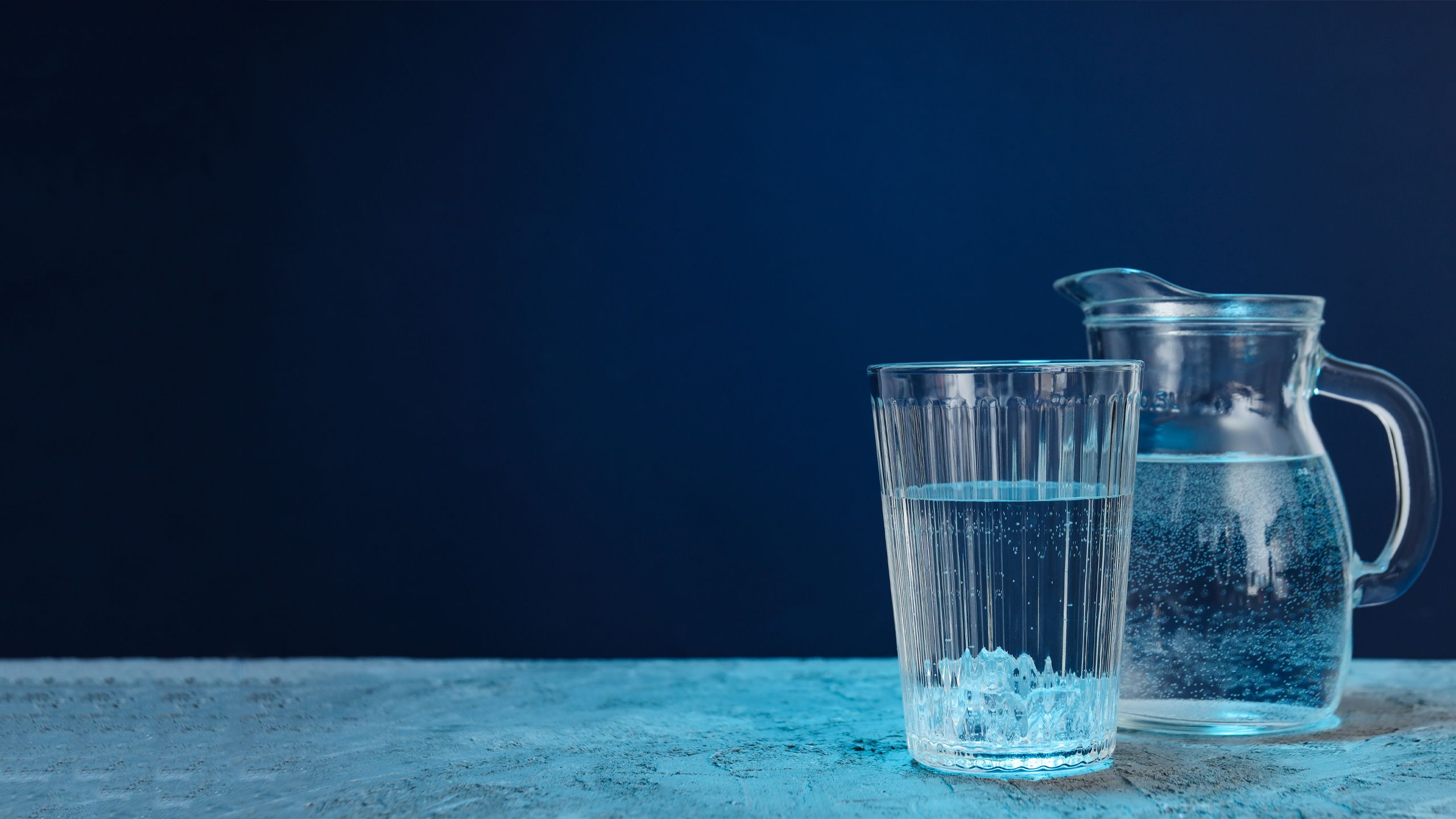 Jug and glass of water on blue textured background
