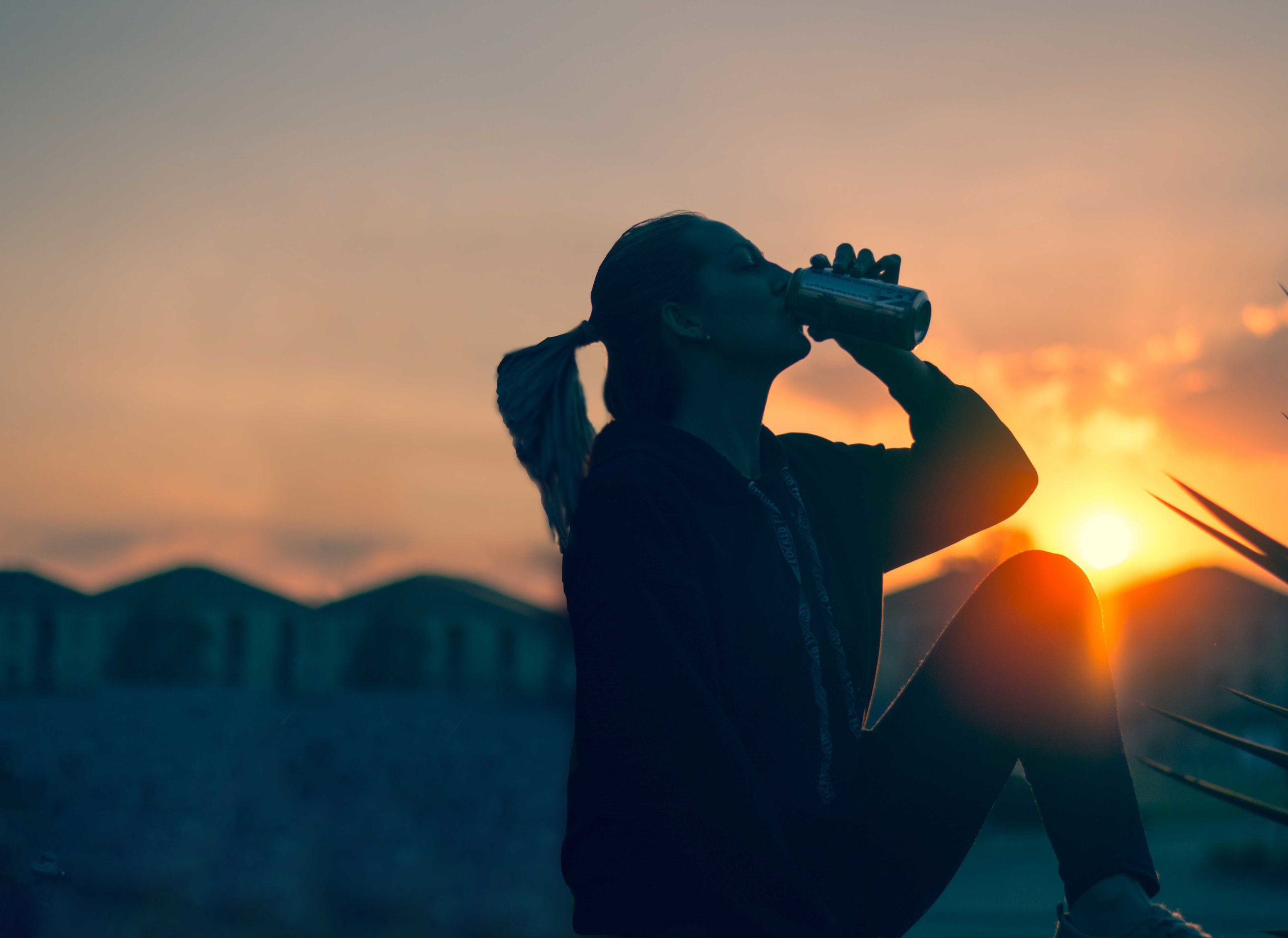 silhouette of woman alone drinking beer at sunset sitting back to back