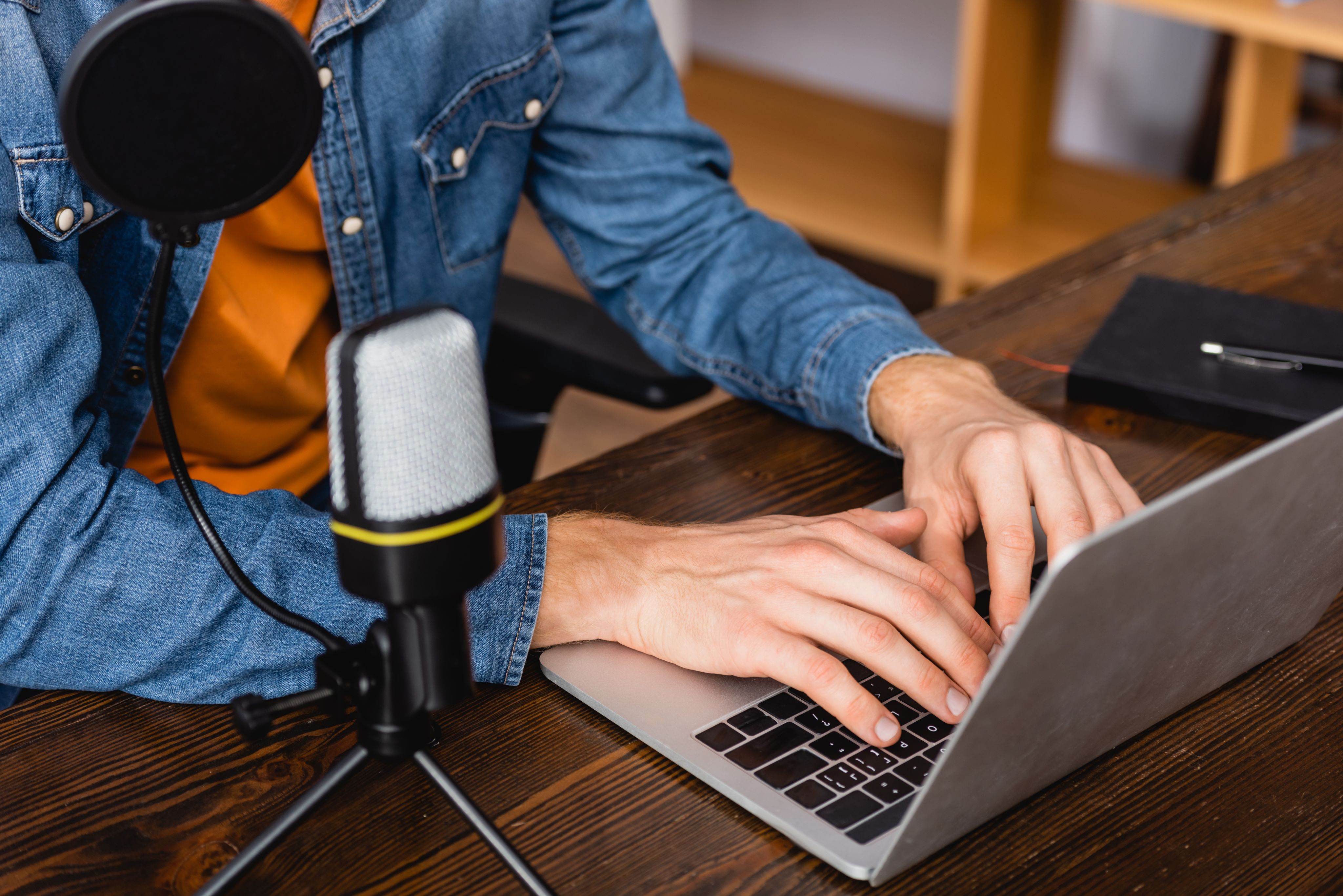 Person seated at desk typing on laptop with a microphone placed next to it.