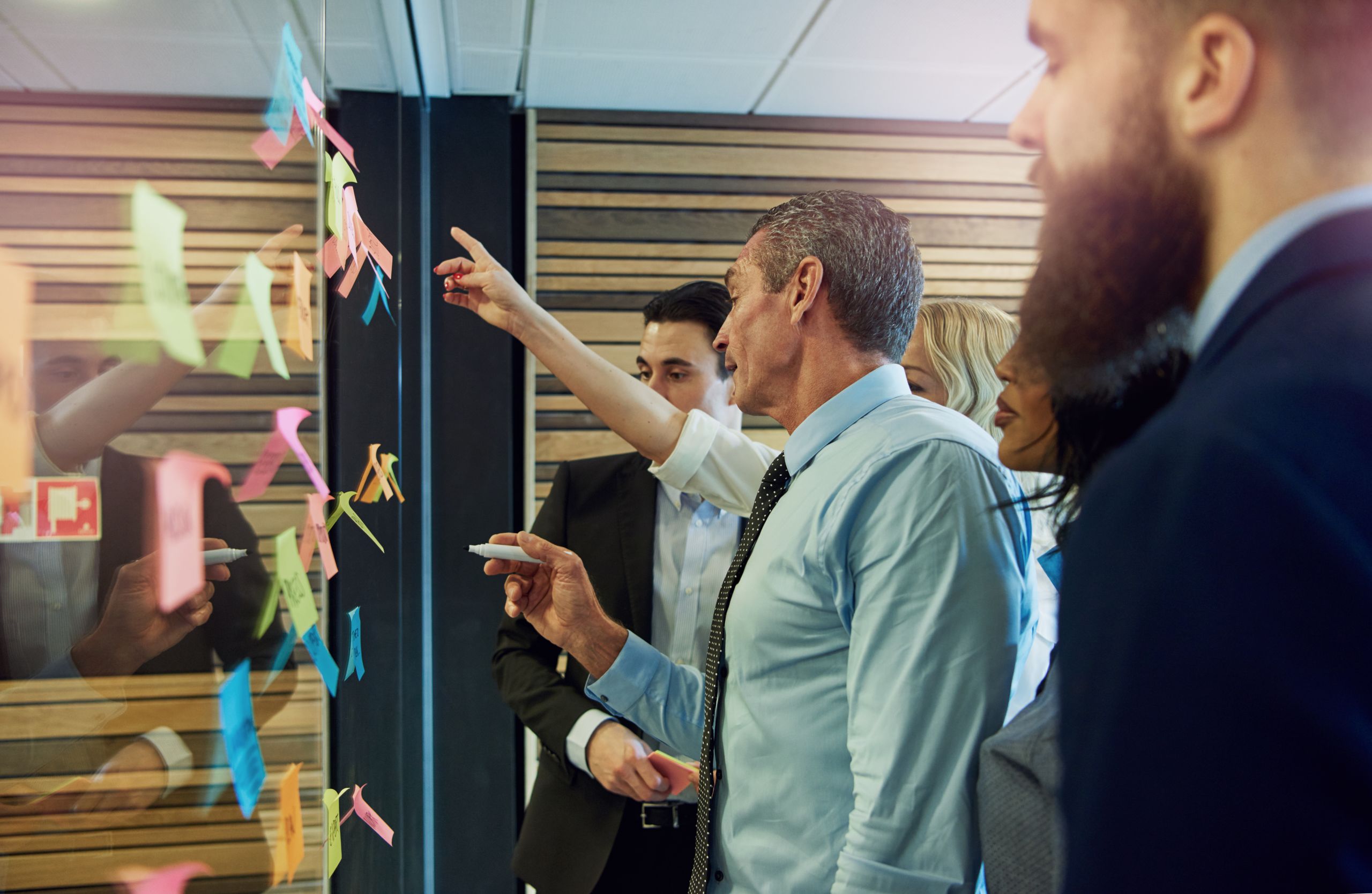 Group of business professionals pointing at coloured post it notes, working together to problem solve