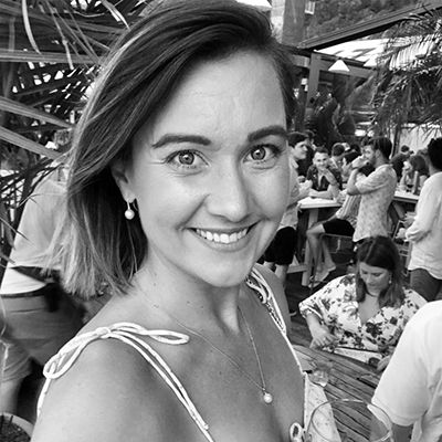 A black-and-white headshot of Elise Harris, a woman with shoulder-length dark hair, smiling while standing with people in the background