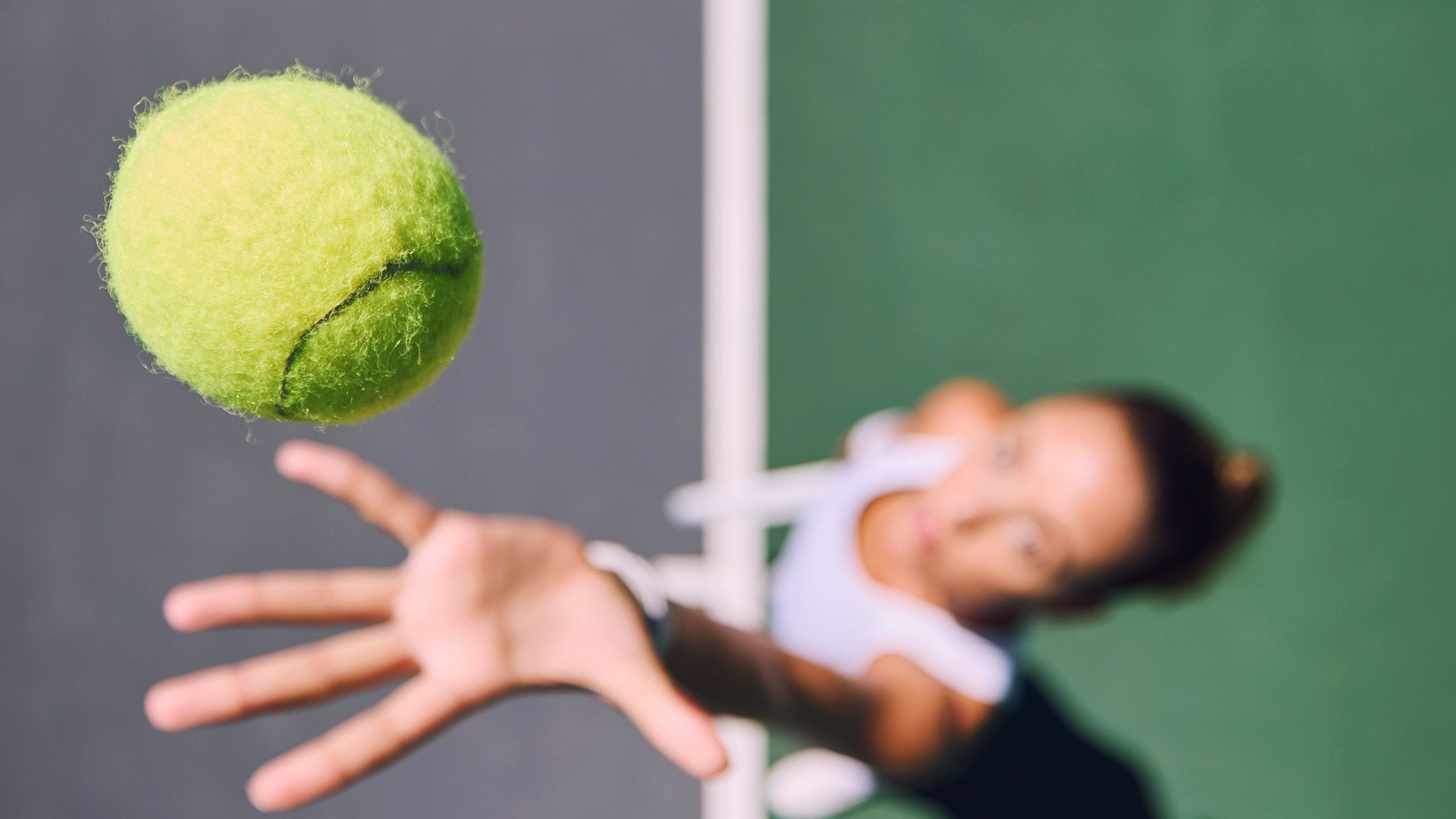 Blurred woman throwing and serving a tennis ball on a court outside from above