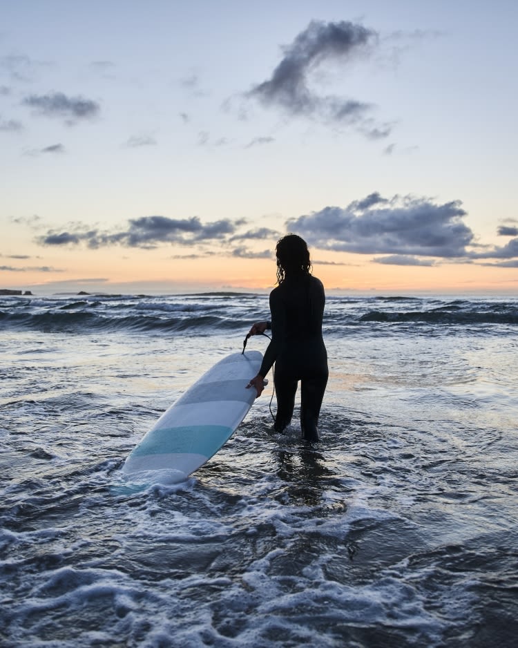 Female surfer entering at the cold ocean water with board and preparing for the training