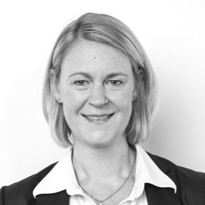 A black-and-white headshot of Lisa Barham, a woman with short light hair, who is smiling while standing against a plain background