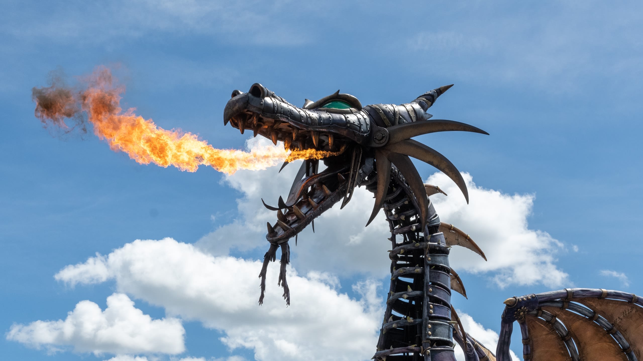 A mechanical dragon breathing fire in front of a cloudy blue sky