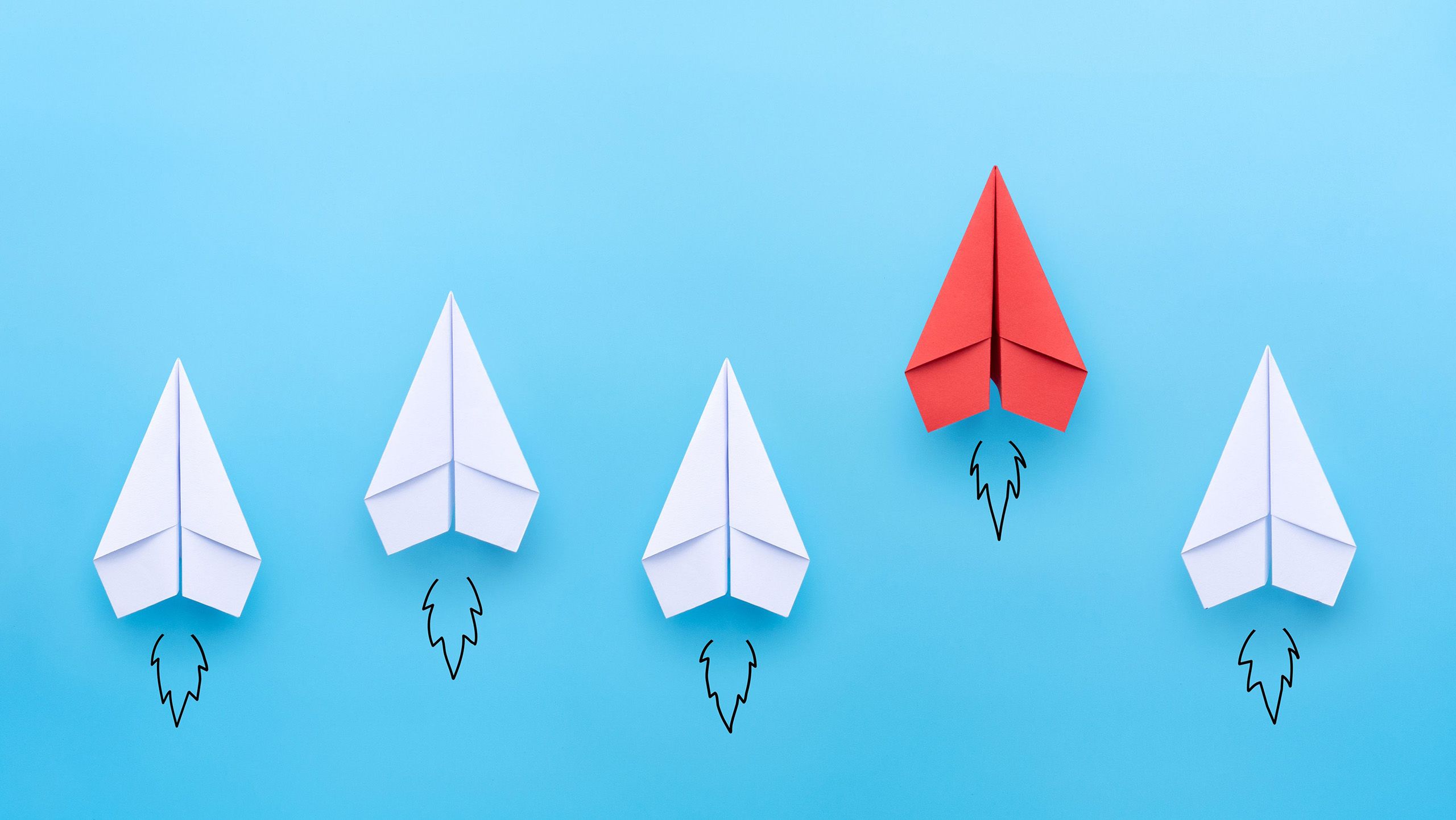 Four white paper airplanes accompanied by one red paper airplane