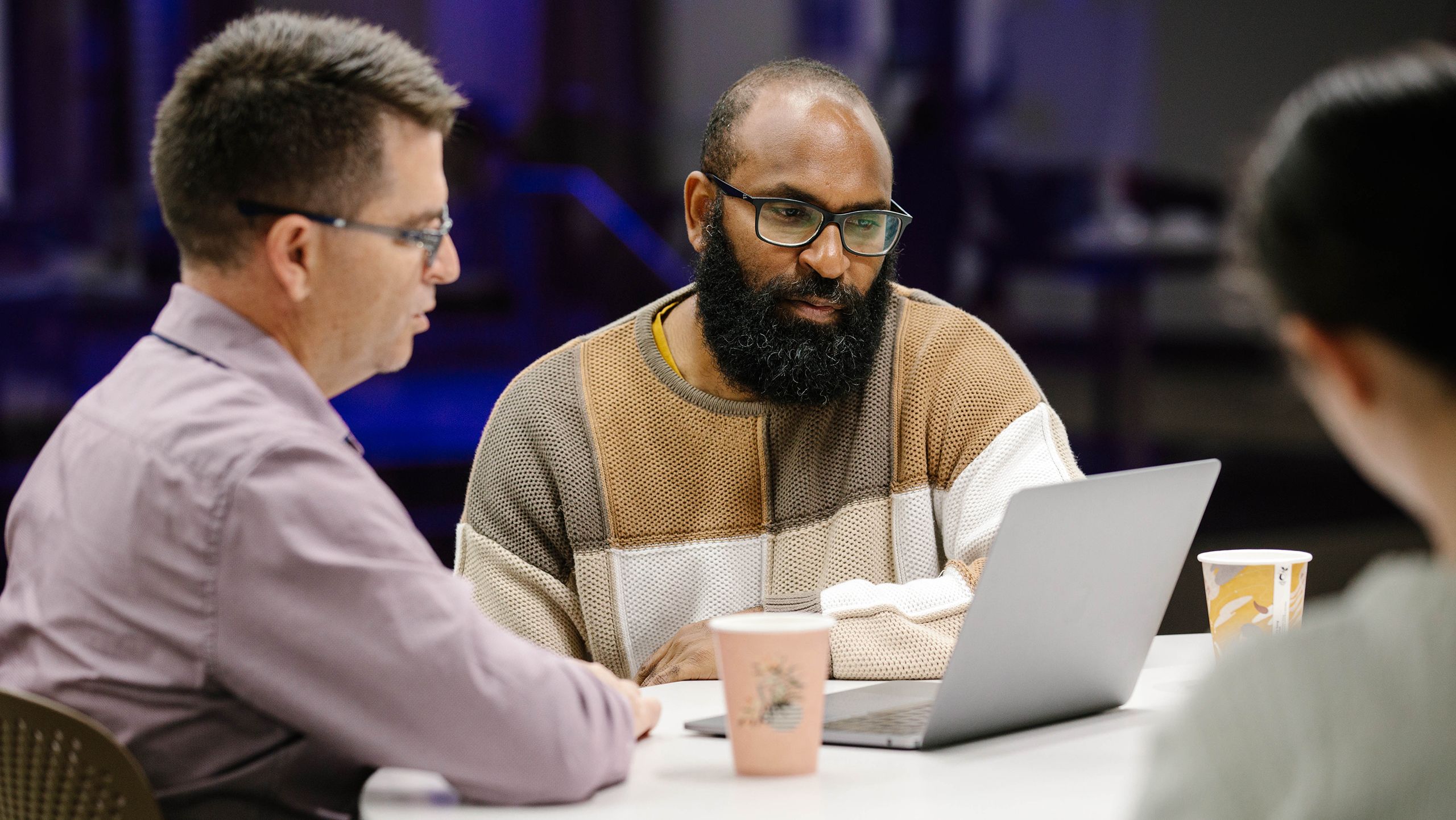 Two people sitting at a table looking down at a laptop