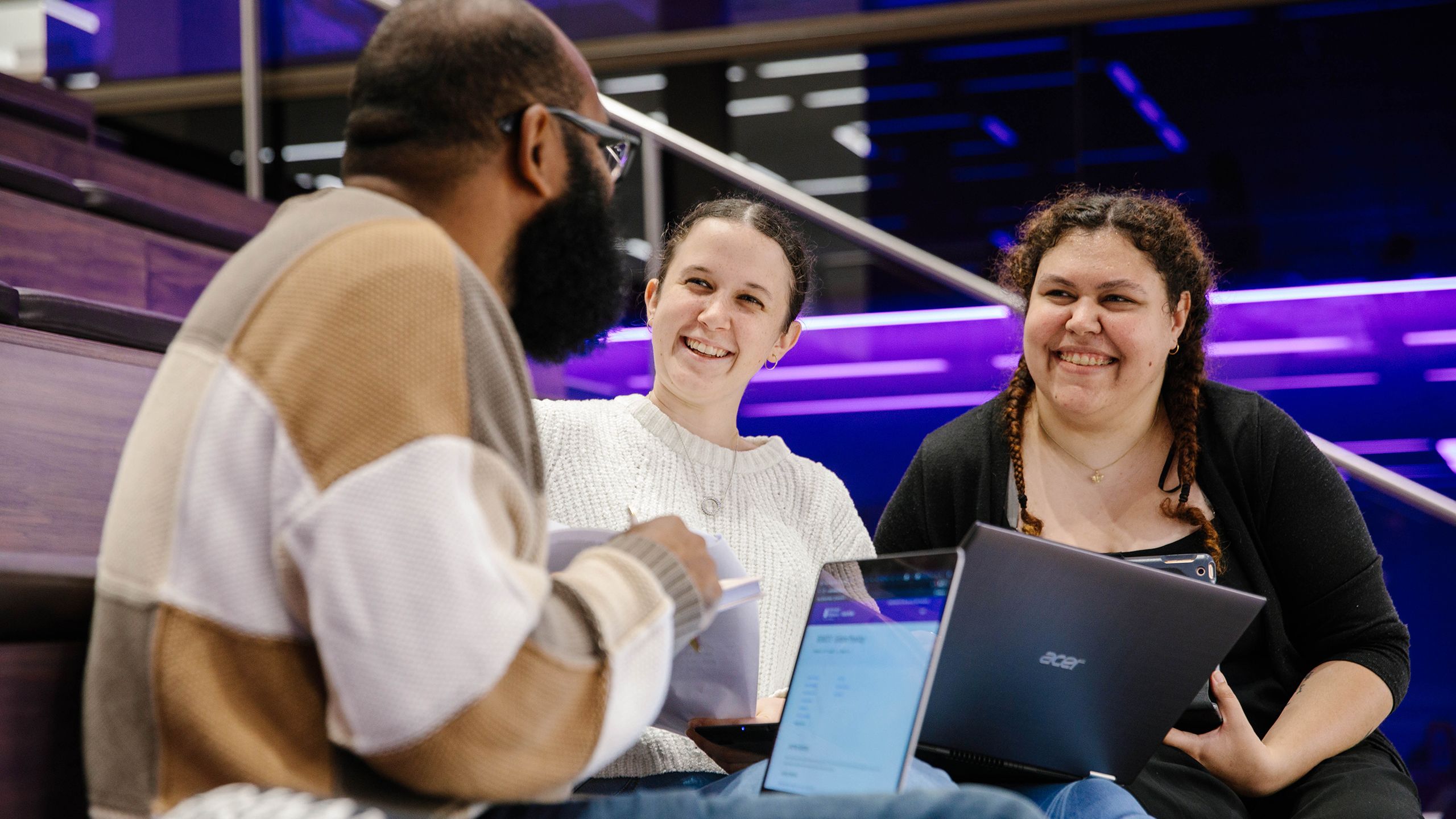 Three students sitting down talking to each other and smiling