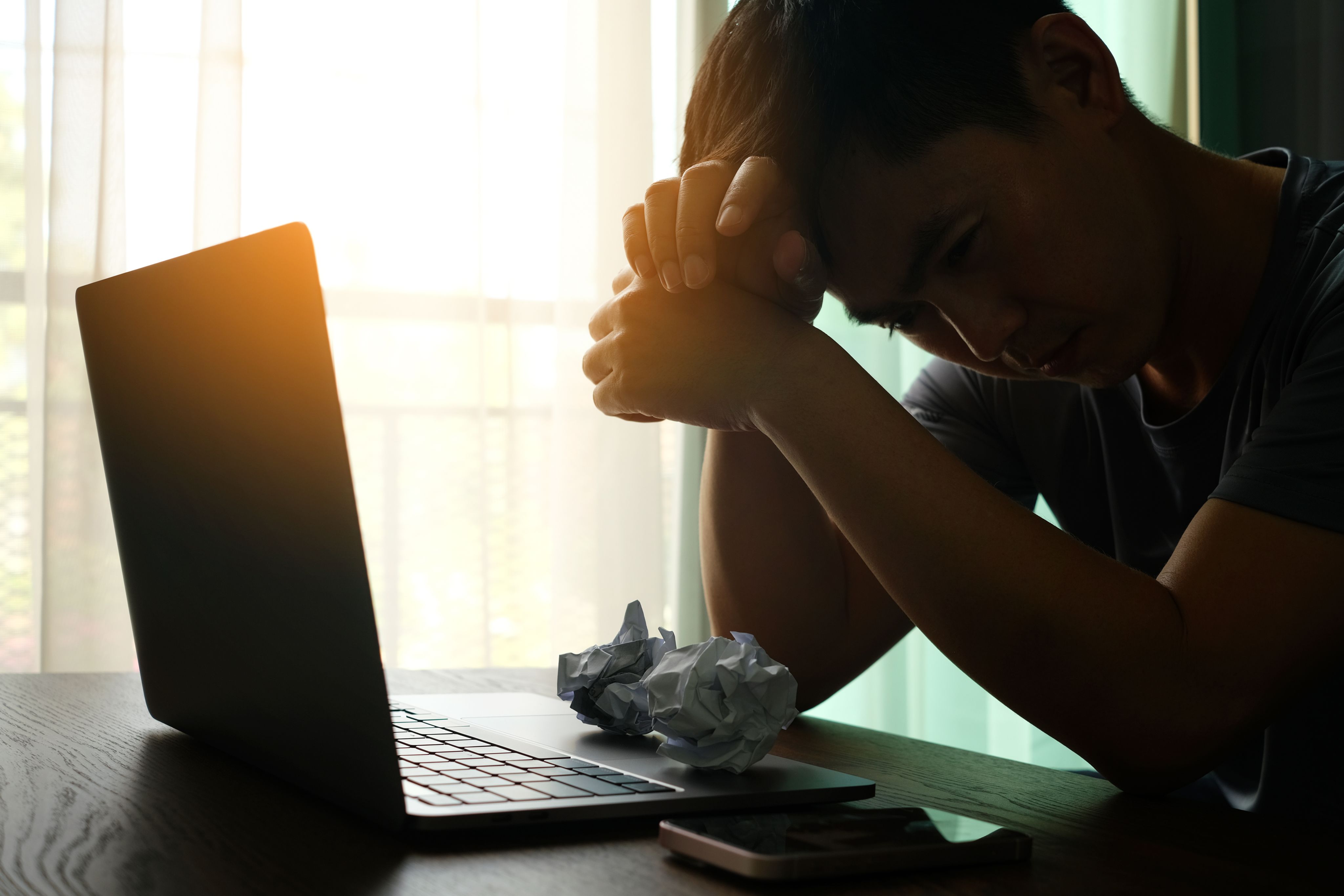Person sitting at desk in front of laptop with their head in their hands
