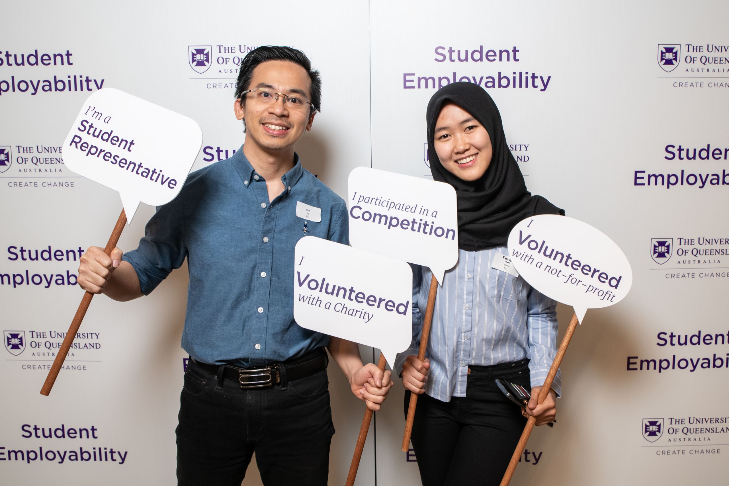 Two students participating in the Employability options at UQ, standing holding signs in front a sign for the program