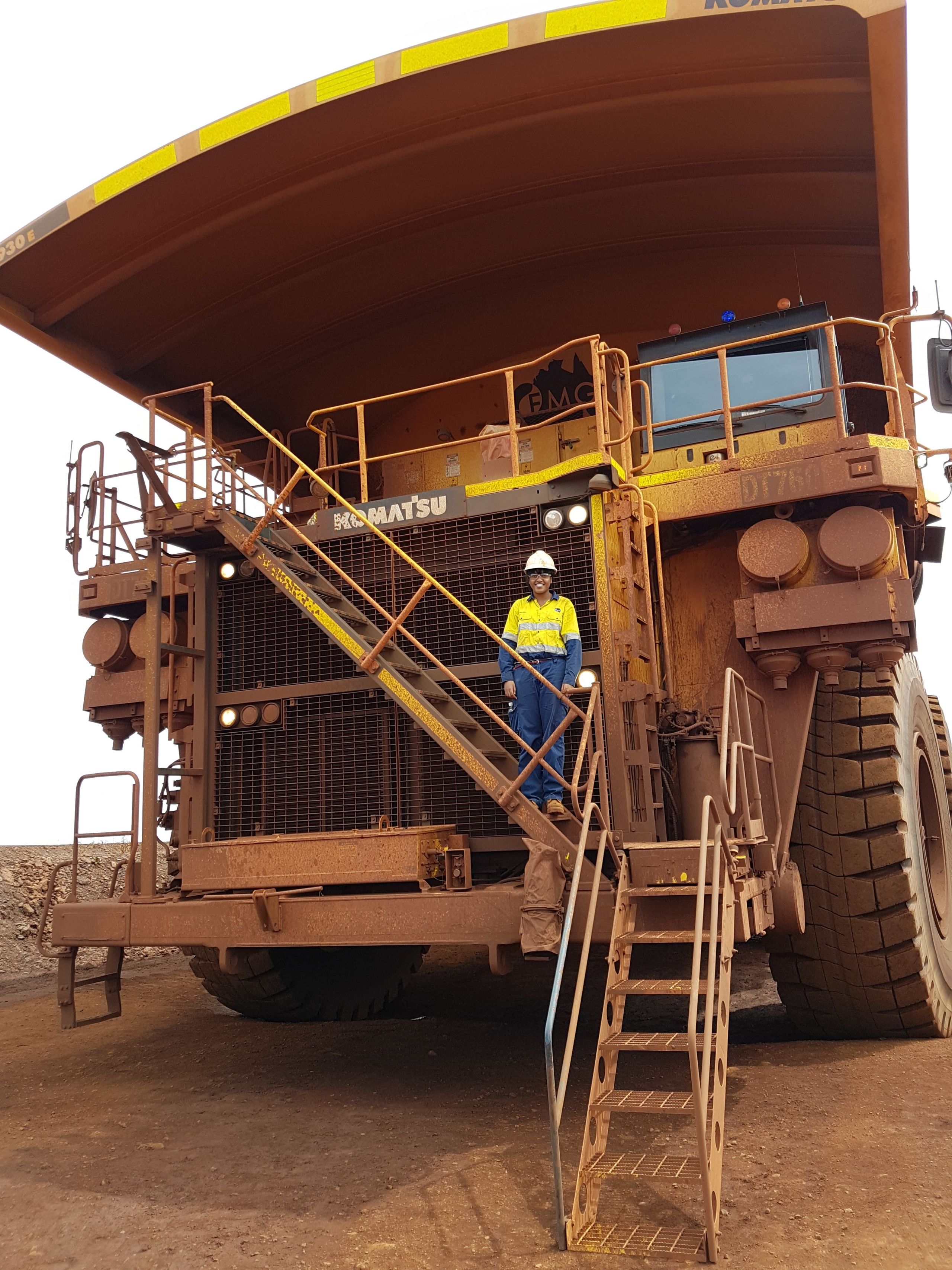 Geethu dwarfed by the huge machine she's standing on during her work with FMG at an iron ore processing facility