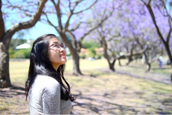 Phuong Tran looking up at the flowering jacaranda trees at UQ.
