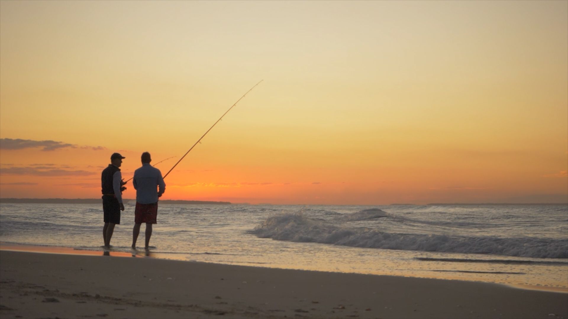 Silhouette of two men fishing on Stradbroke Island at sunset.