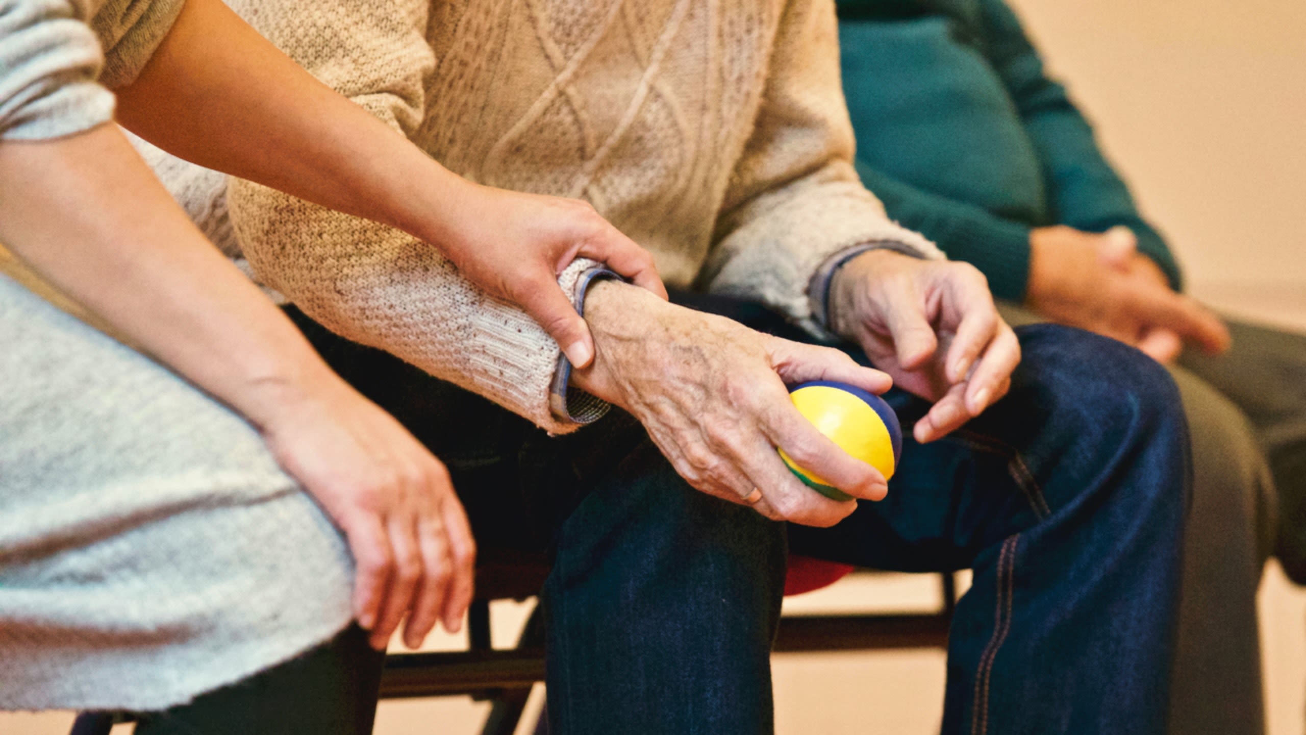 Seated man holding squeeze ball, with woman sitting next to him with her hand on his wrist
