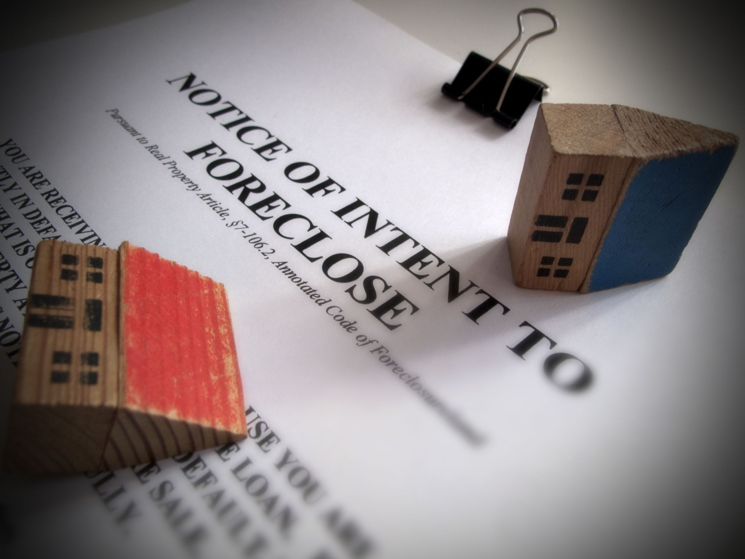 Foreclosure notice with wooden models of houses turned on their side lying on it