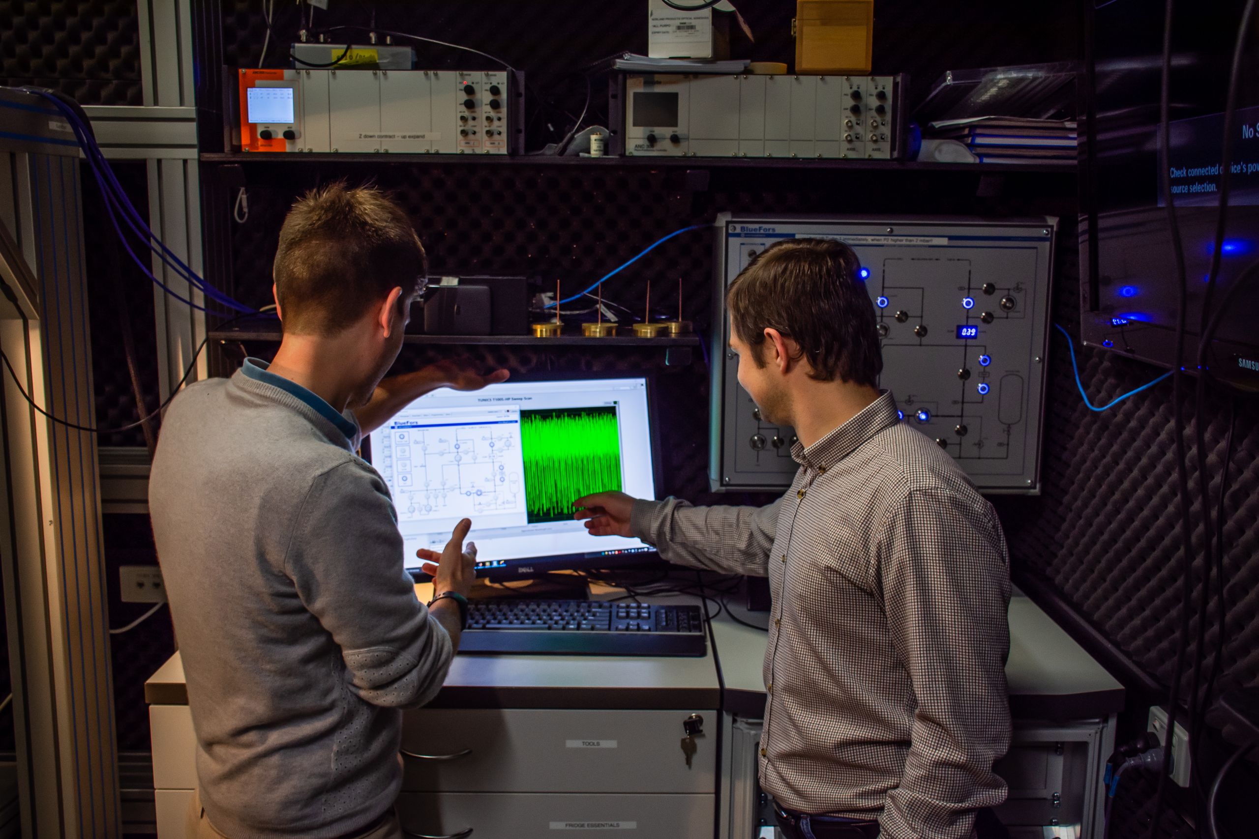 Two scienists looking at a computer screen of graphics from ultra cold refrigerator performance.