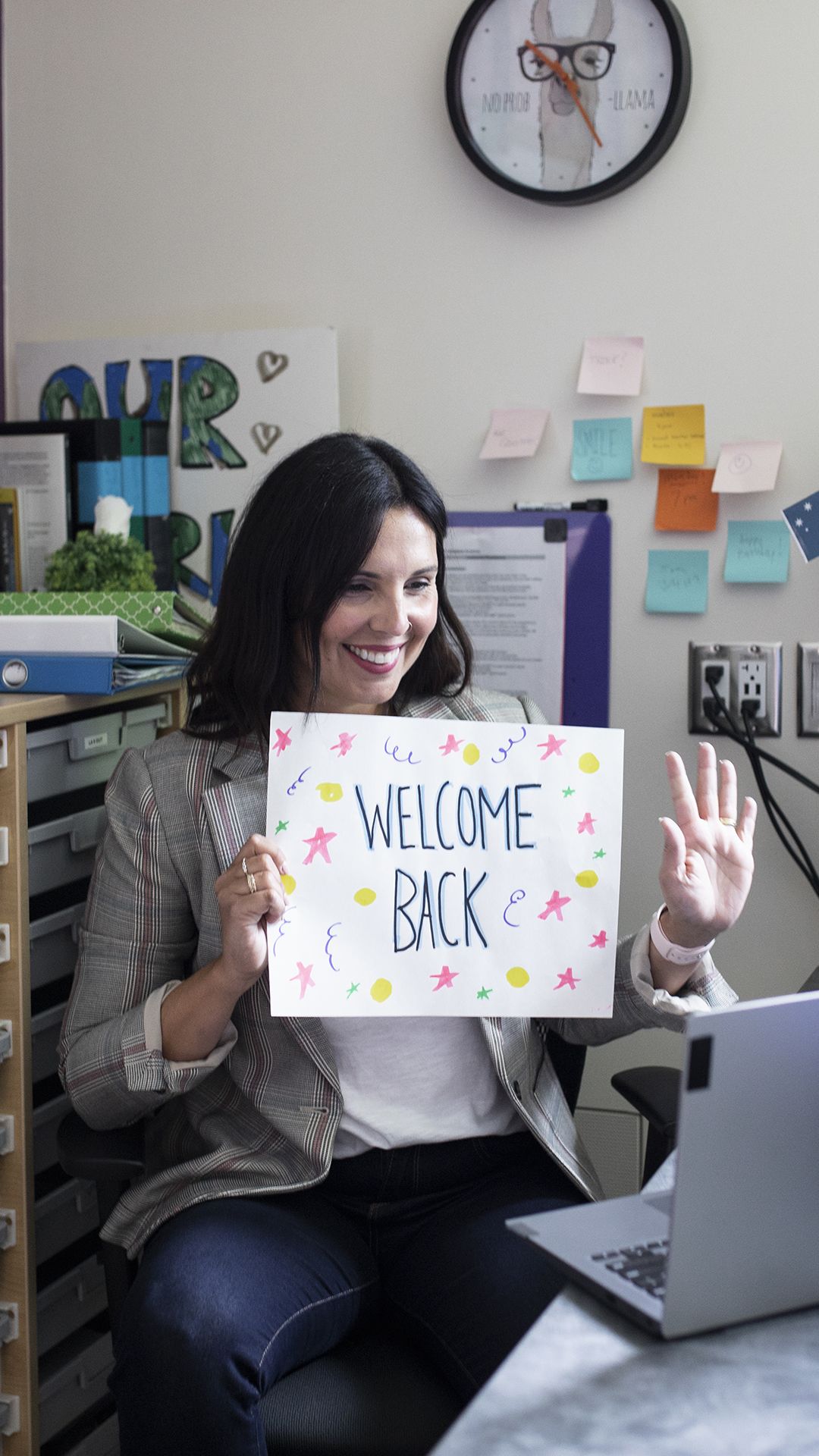 Teacher holding up 'Welcome Back' sign to students online.