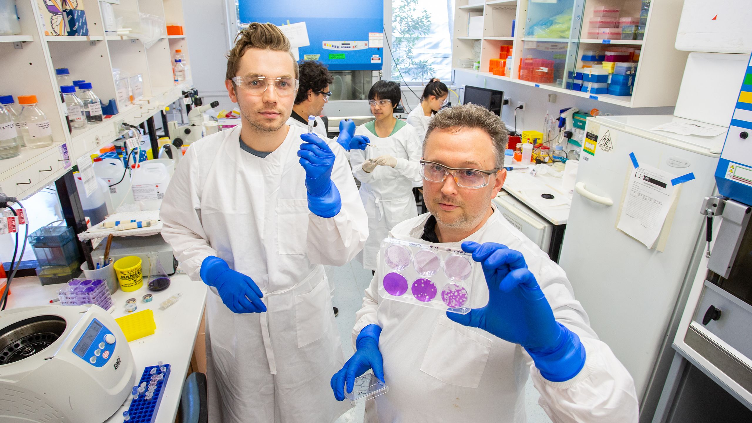 Dr David Muller and associates in the lab, with Dr Muller holding up a container with purple-coloured spheres