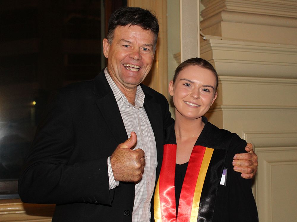 Anna standing next to her father with his thumbs up. She's wearing an Indigenous grad sash