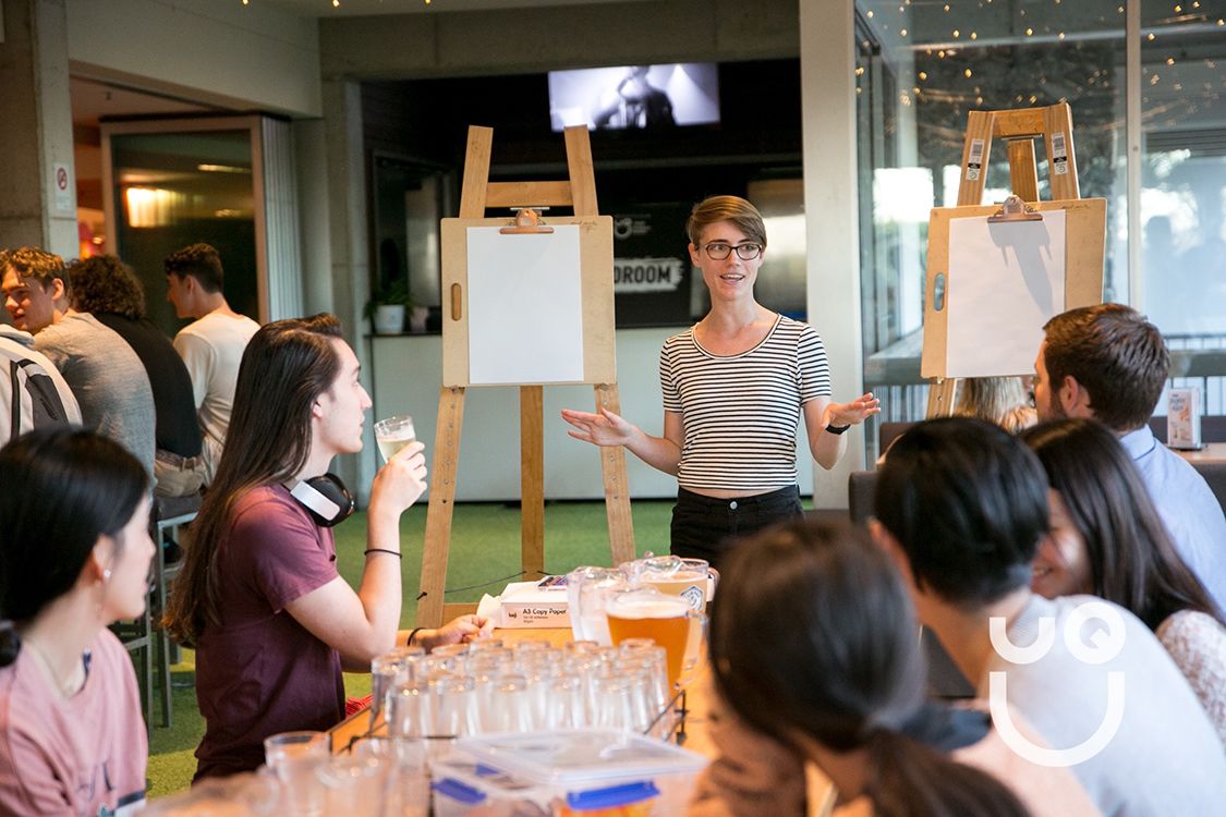 Mx Bradford standing at an easel, with people sitting in front of her at a table with beer on it
