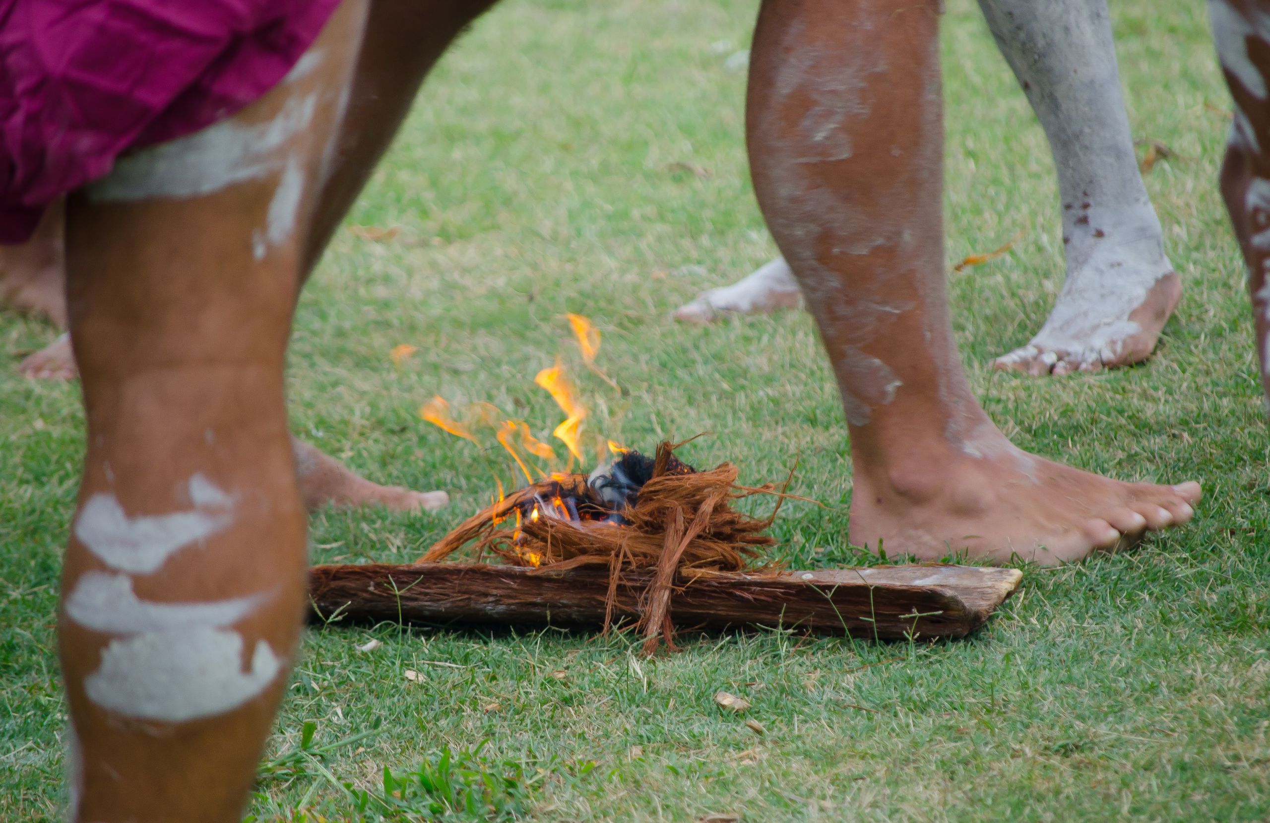Legs of Indigenous performers surround the burning bark for a smoking ceremony