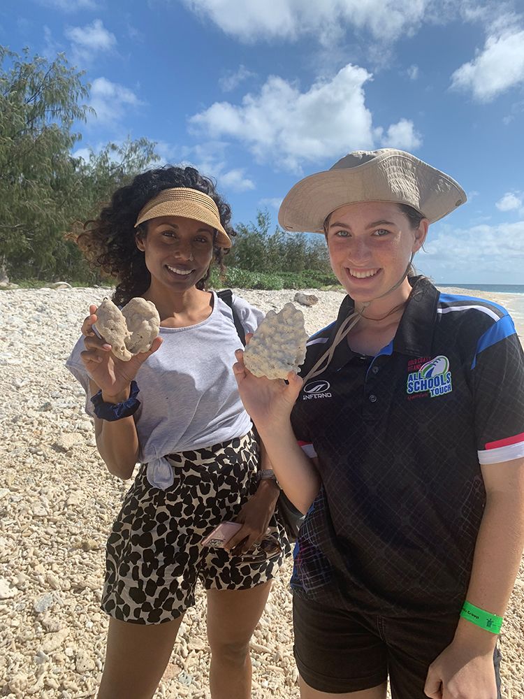 Dr Sonia Shah and Cadence Taylor standing on a beach holding dried coral