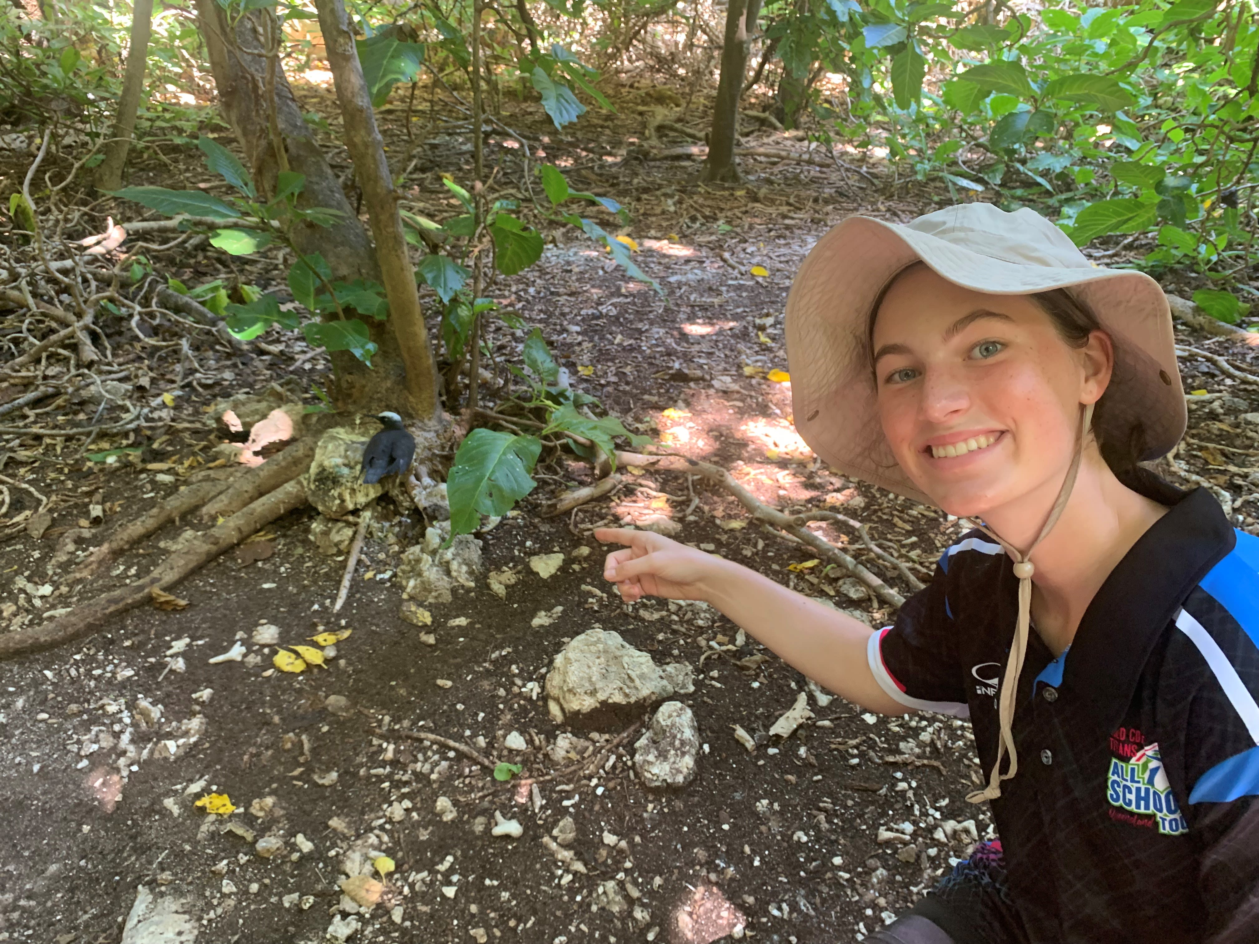 Cadence Taylor kneeling and pointing at a bird that is sitting on the ground