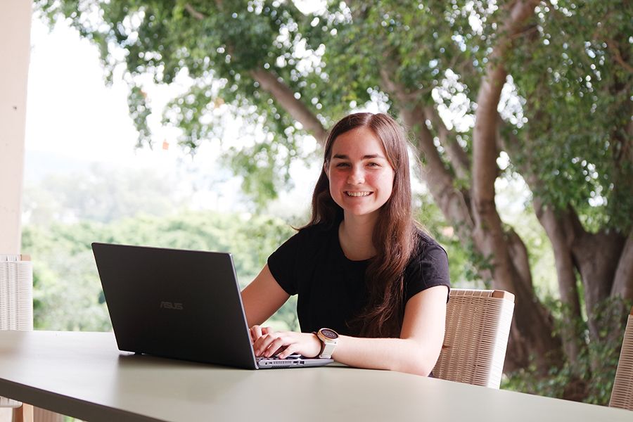 A young smiling woman sitting at a table outdoors with a laptop