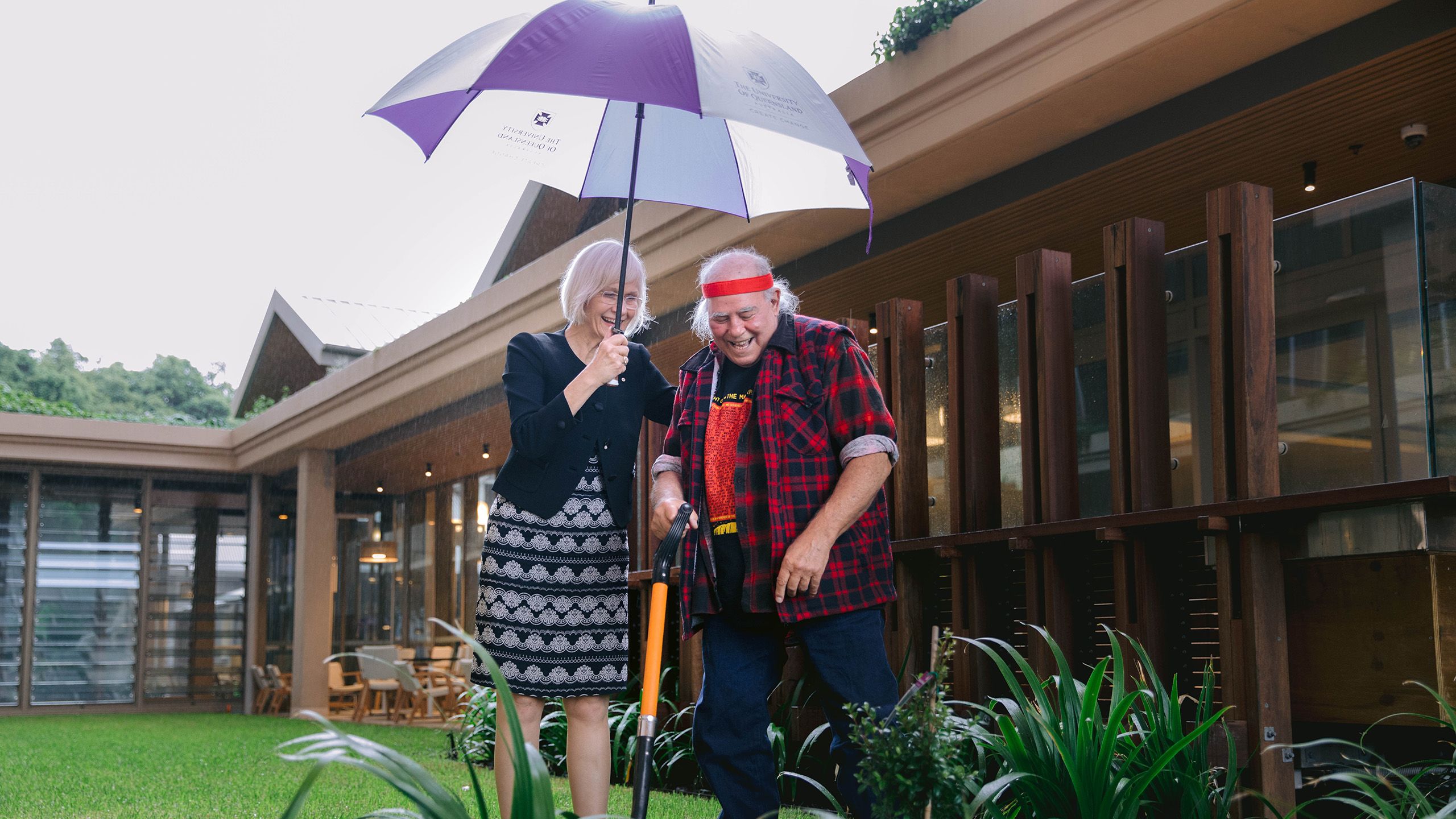 Vice-Chancellor Professor Deborah Terry holding an umbrella over herself and Kev Carmody