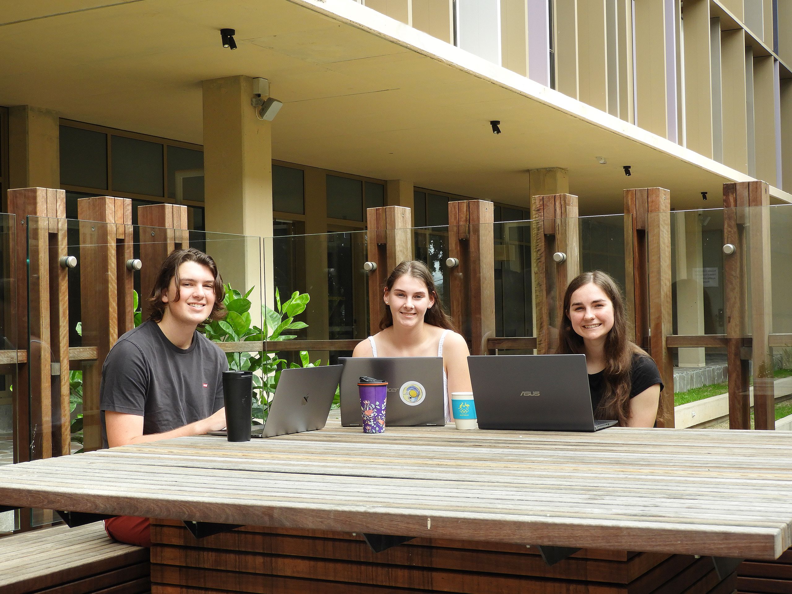 Three young people sitting at a table with laptops and smiling