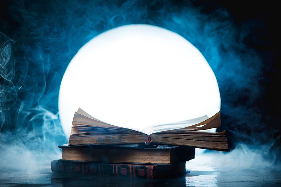 A stack of three books on a surface covered in fog and backlit by a moon-shaped light. The top book is open.