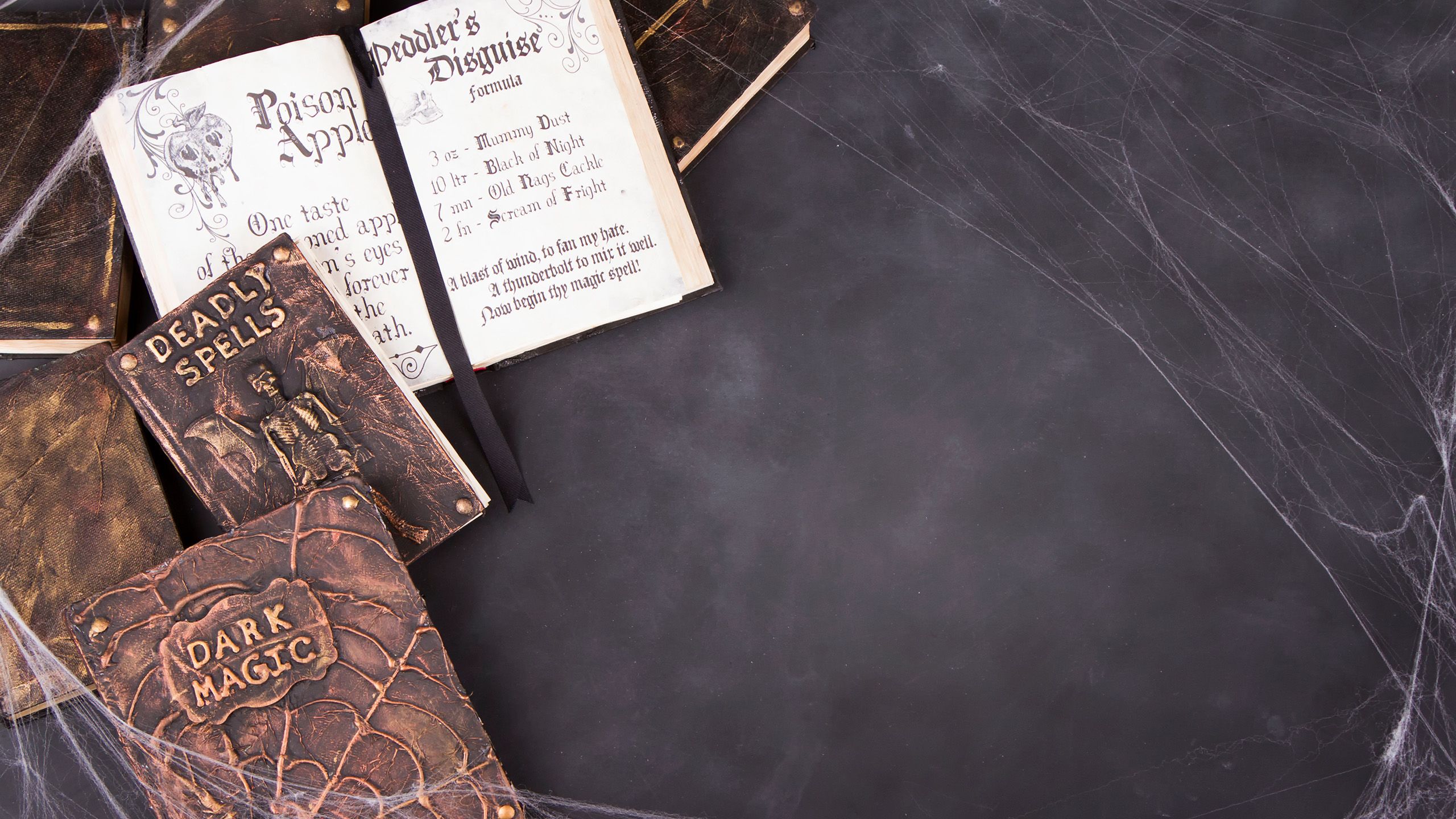 A dark magic book and a deadly spells book lying on a dark surface covered in cobwebs.
