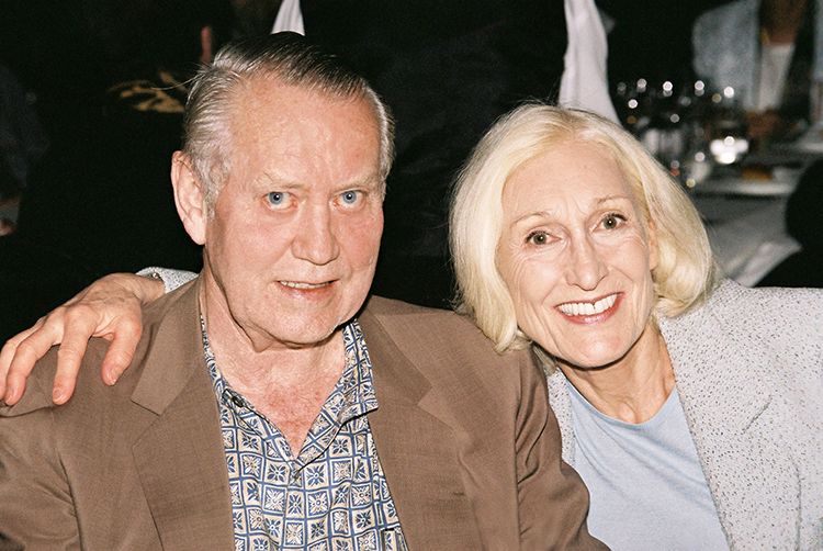 Chuck and Helga Feeney sitting down and smiling at the camera. Helga has her arm resting across Chuck's shoulders.