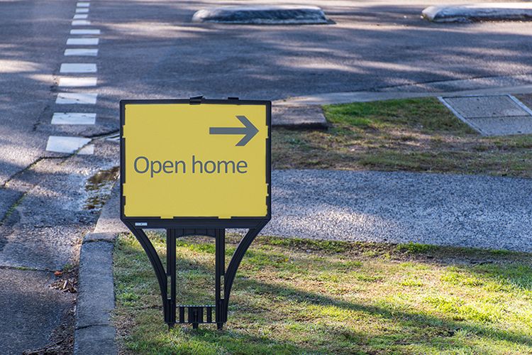 A rectangular 'Open Home' sign on a street corner with an arrow pointing down a road