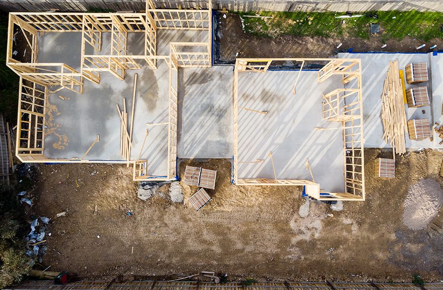An aerial view of a house being constructed. A concrete slab has been laid and the frame is being assembled.