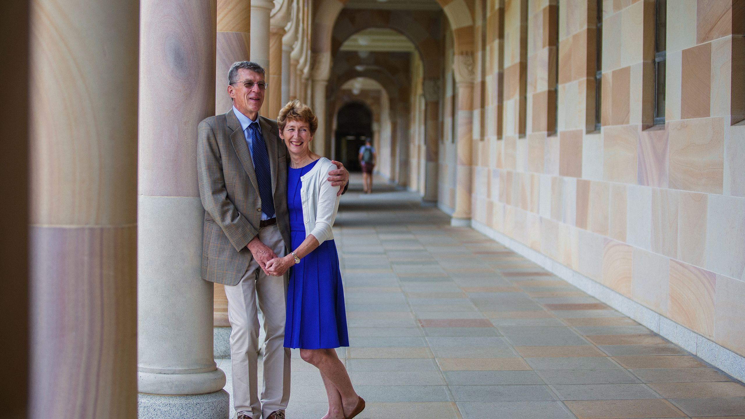 Ian and Caroline Frazer with their arms around each other's shoulders in a sandstone corridor