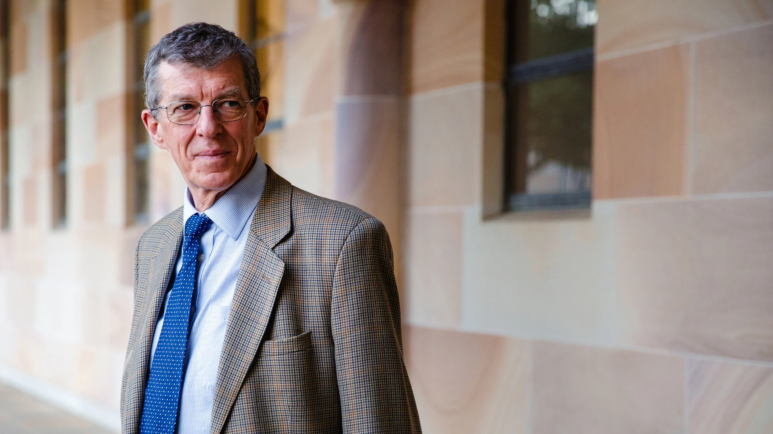 Ian Frazer standing in front of a sandstone building wearing a suit and tie