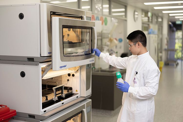 A man wearing a lab coat and safety goggles opening the door of a large piece of scientific equipment in a laboratory