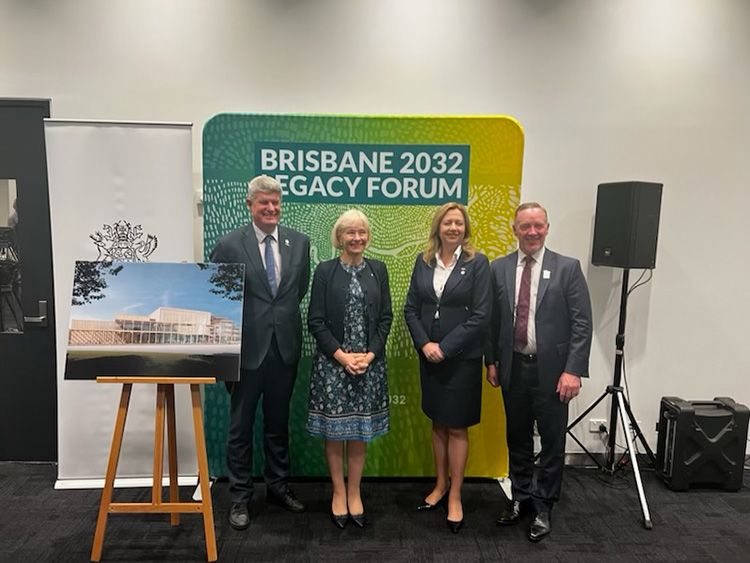 Four people wearing business attire in front of a 'Brisbane 2032 Legacy Forum' sign and standing next to an artist's impression of a modern building