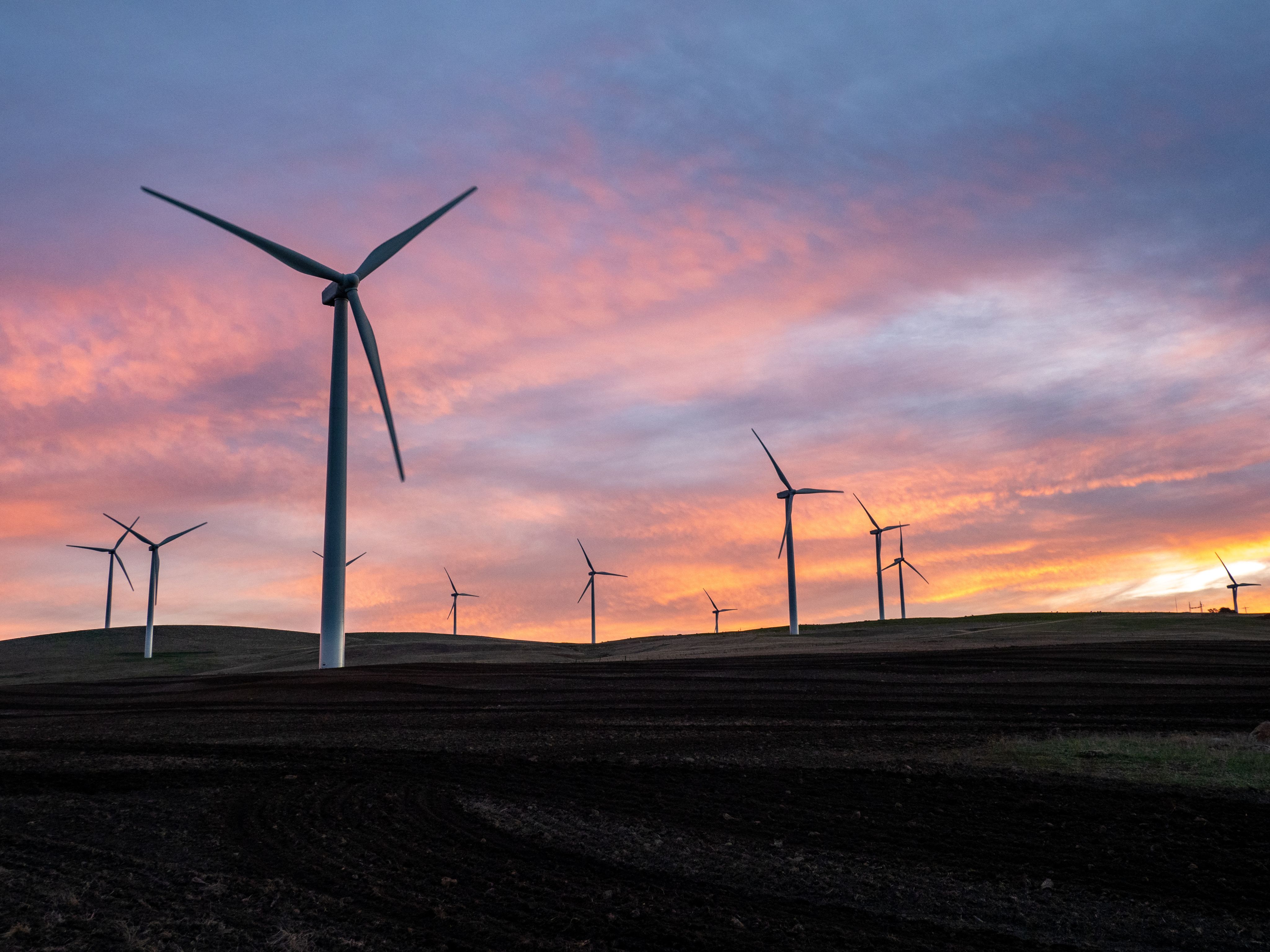 Ten wind turbines on grass hills at sunset