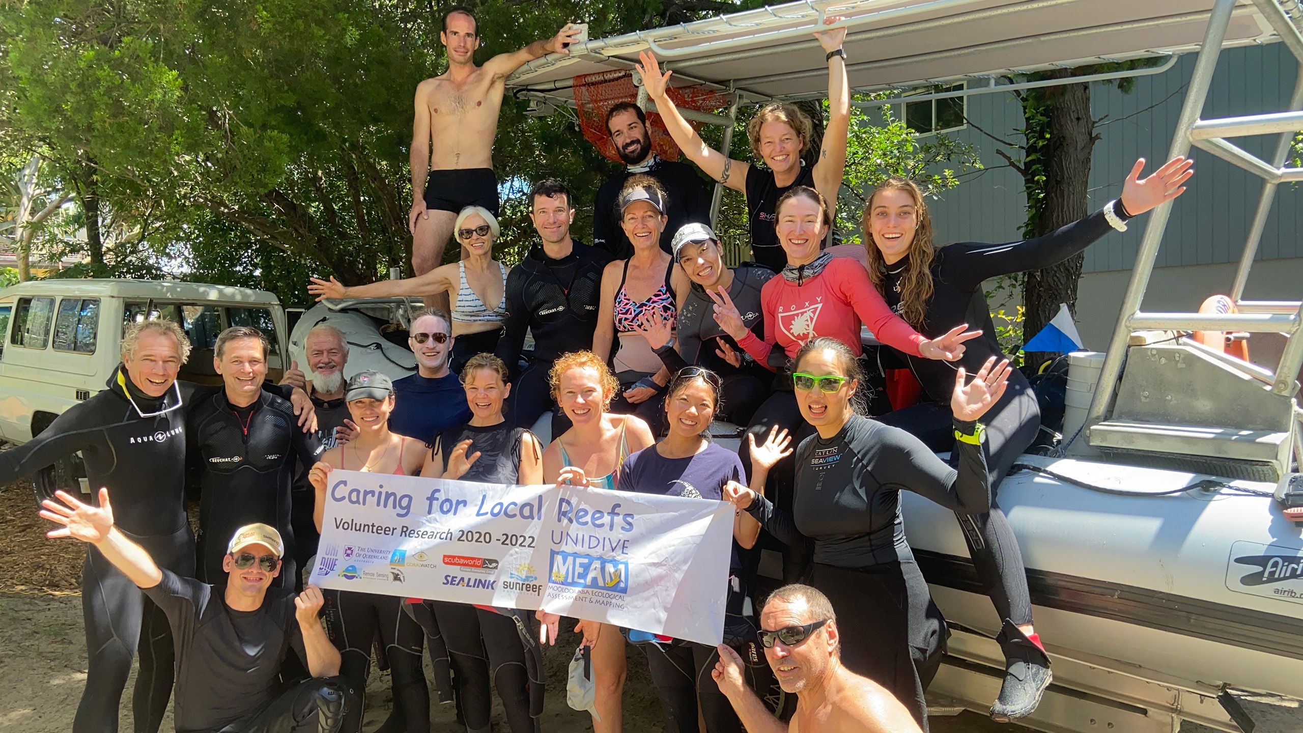 A group of people in swimwear on a beach holding a 'Caring for Local Reefs' banner