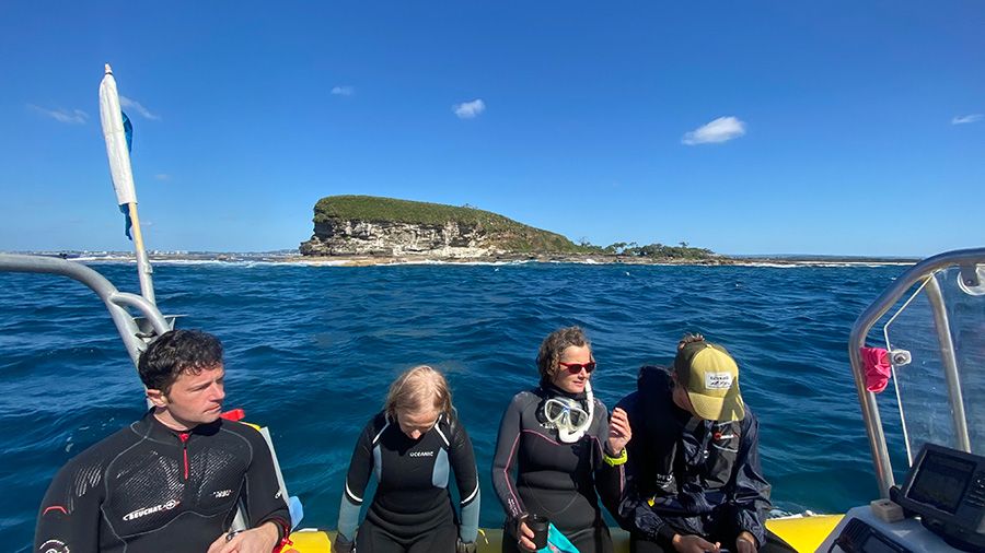 A group of people wearing wetsuits sitting on the edge of a small boat at sea