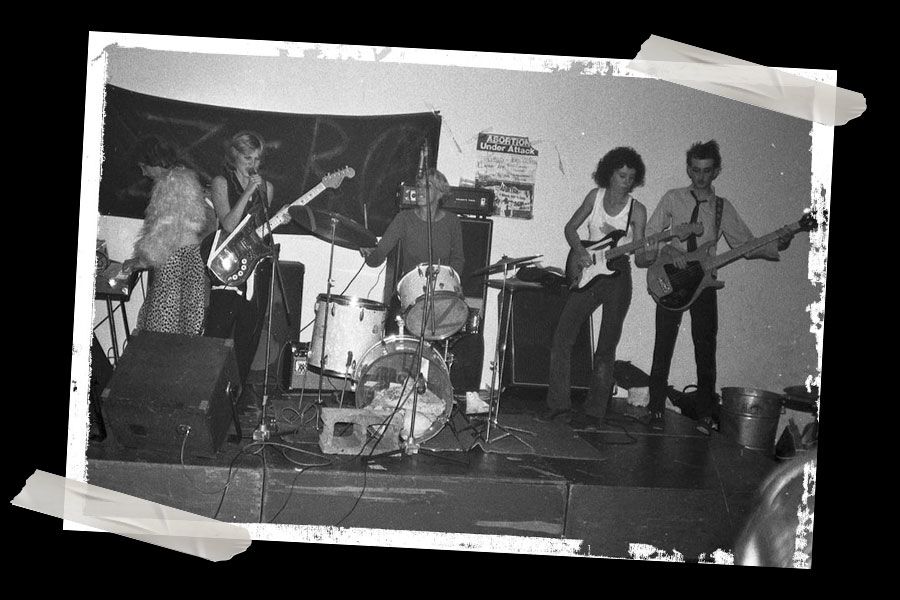 A black and white image of a band on stage with keyboardist, guitarists and drummer.
