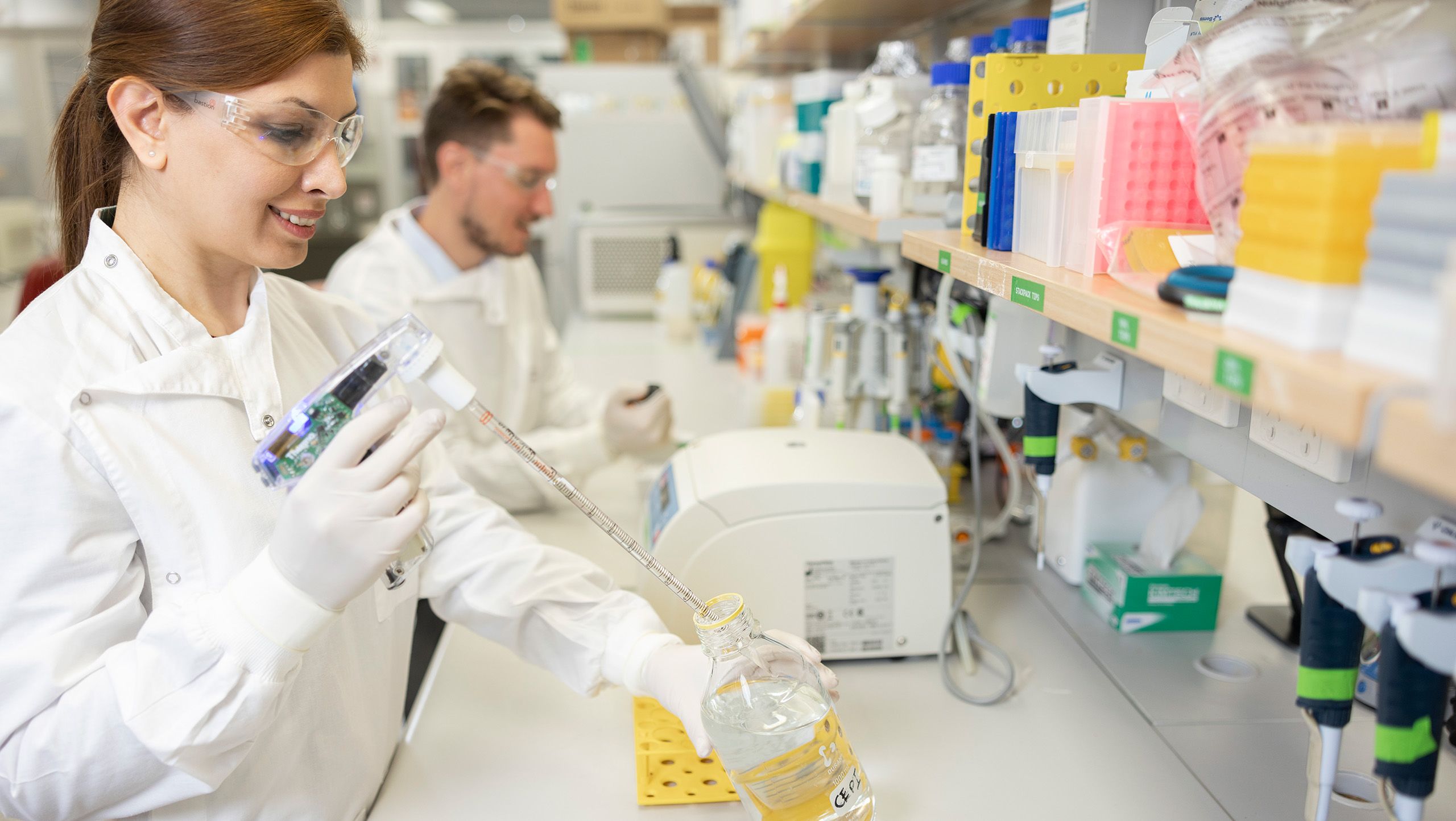 Two scientists measuring liquid and using scientific equipment at a desk in a laboratory