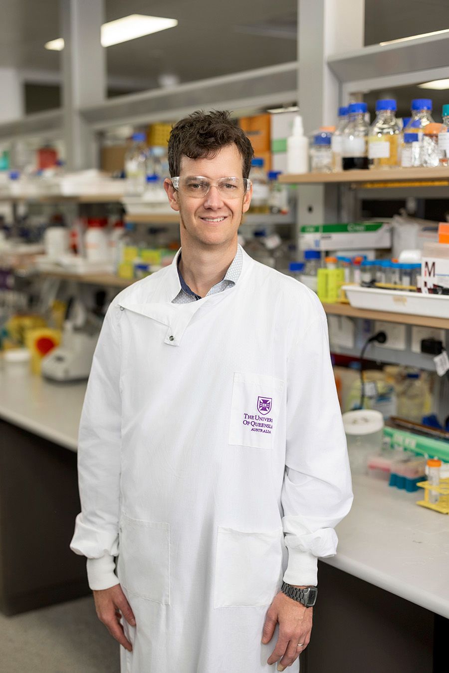 Keith Chappell wearing a lab coat and safety goggles while standing in a science laboratory in front of a long desk and shelves
