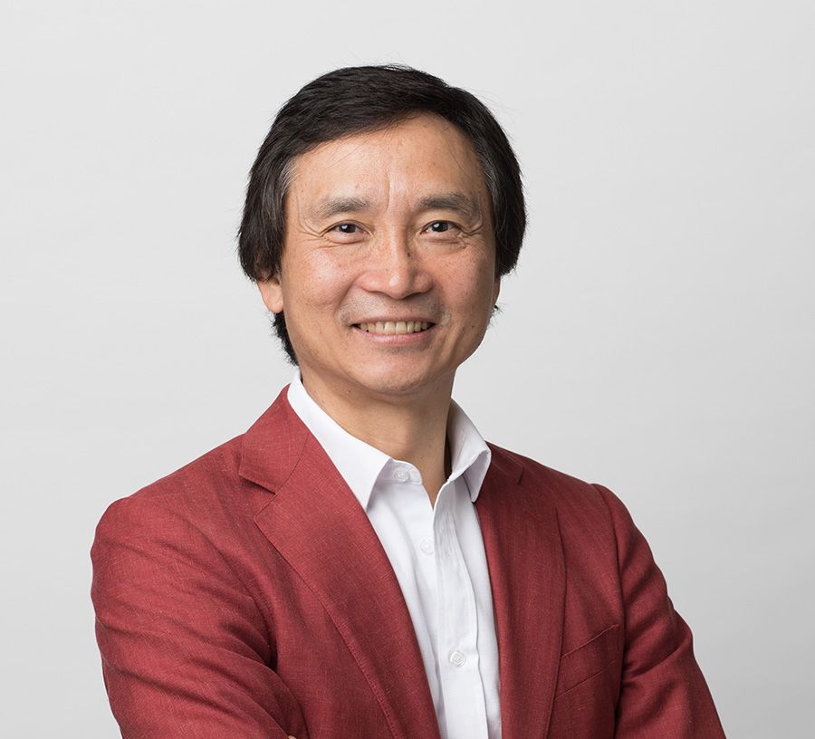 Headshot of Li Cunxin in front of a plain white background, wearing a white collared shirt and maroon jacket.