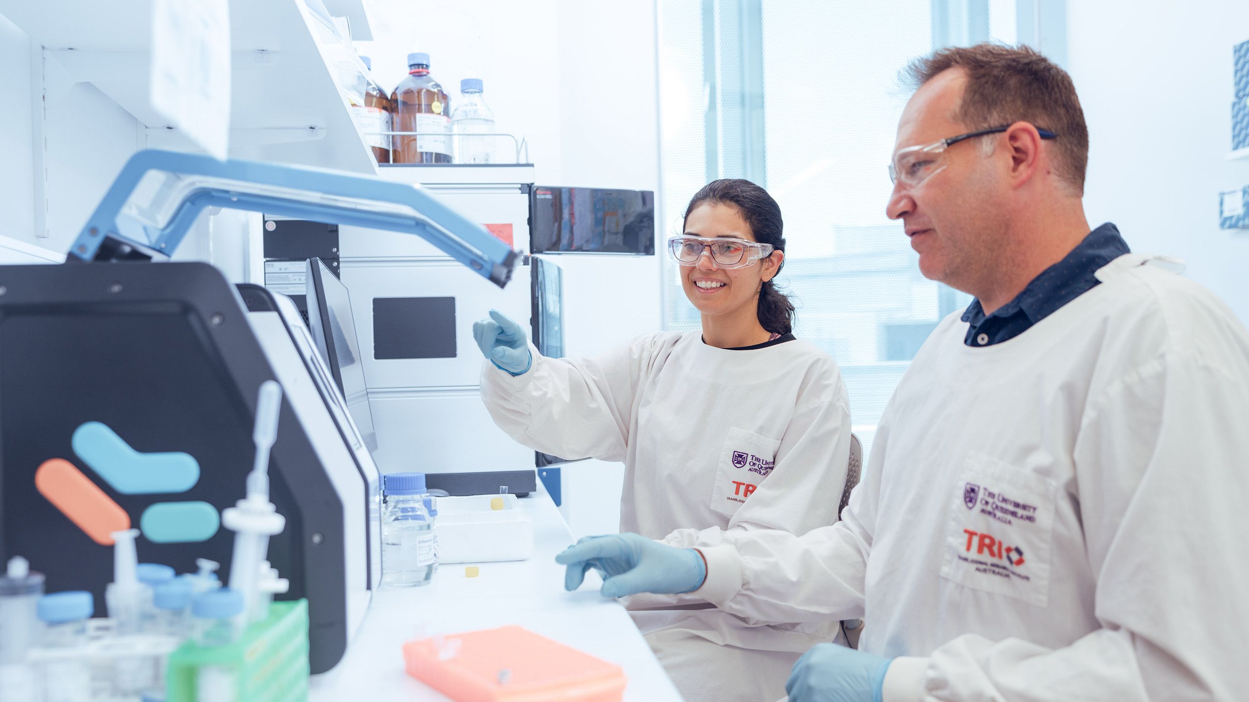 Two people in a science laboratory wearing lab coats while operating equipment