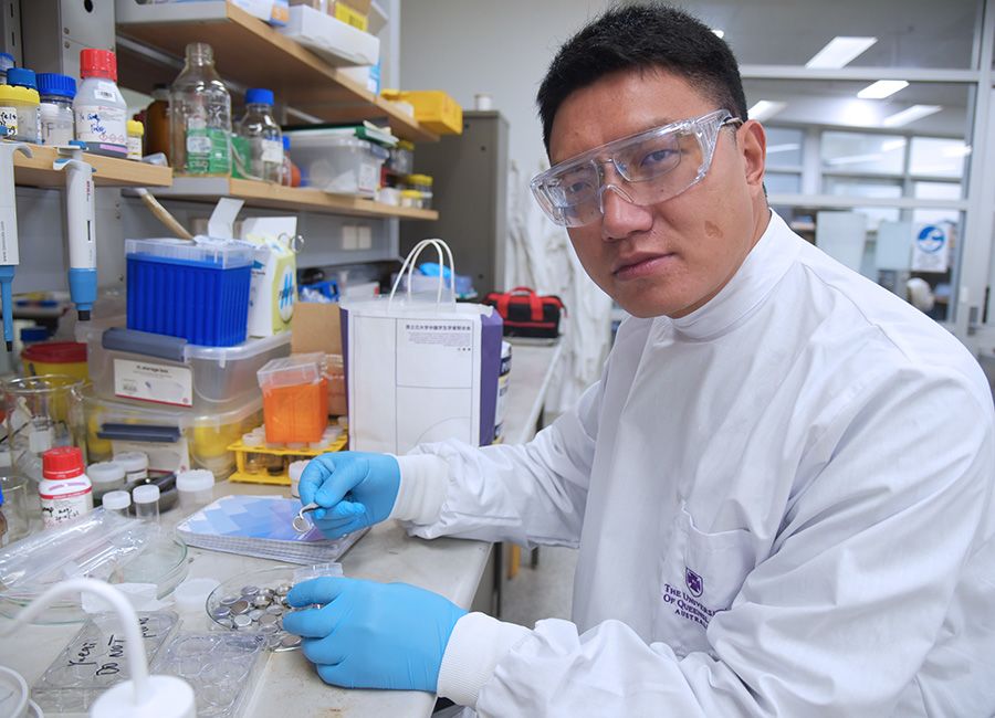 A man in a laboratory wearing a white lab coat, blue gloves and protective glasses