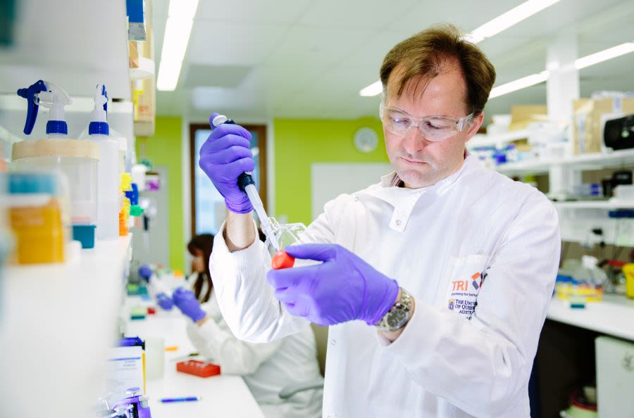 A person wearing a lab coat and safety glasses uses a pipette