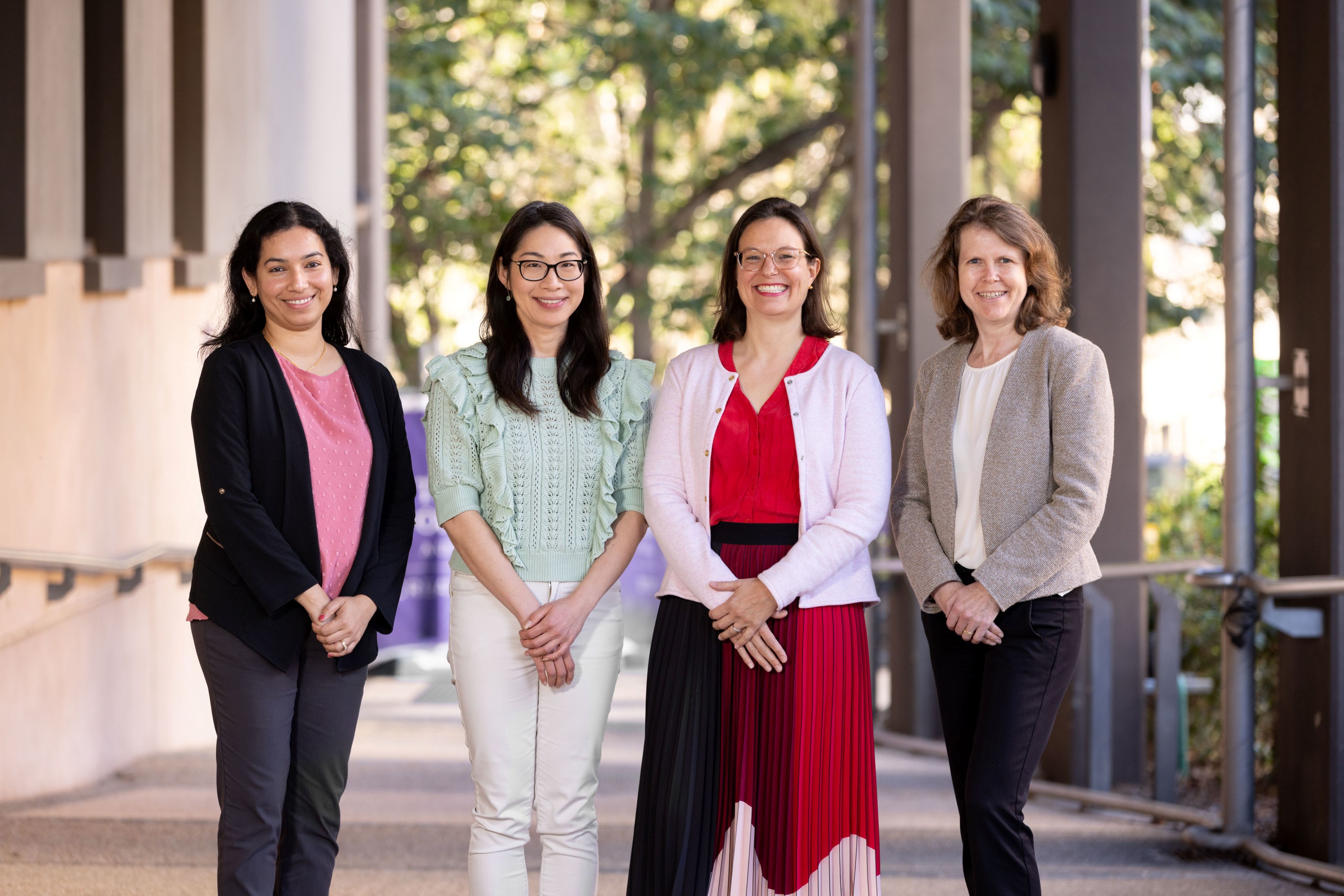 Four smiling women standing outside beneath an undercover walkway in a group.